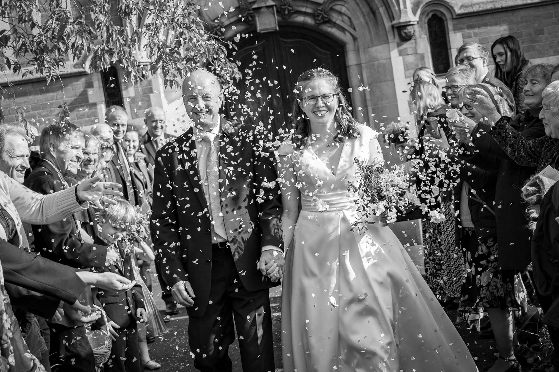 A black and white photo of a bride and groom being showered with confetti.