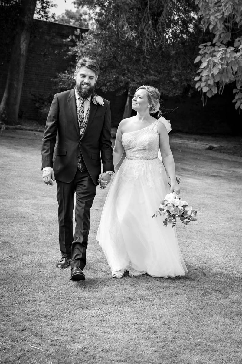 A bride and groom are walking in a park holding hands.