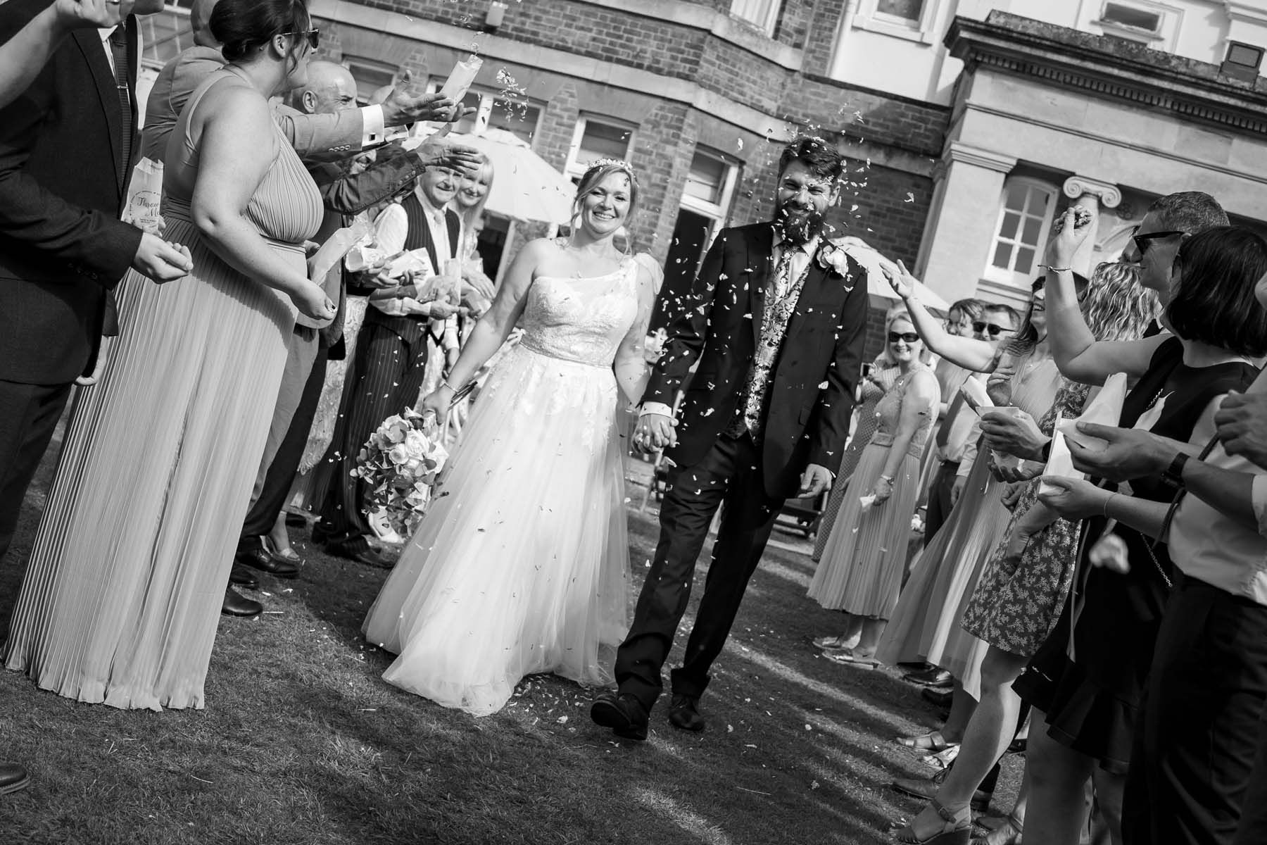 A bride and groom are walking through a crowd of people throwing confetti at them.