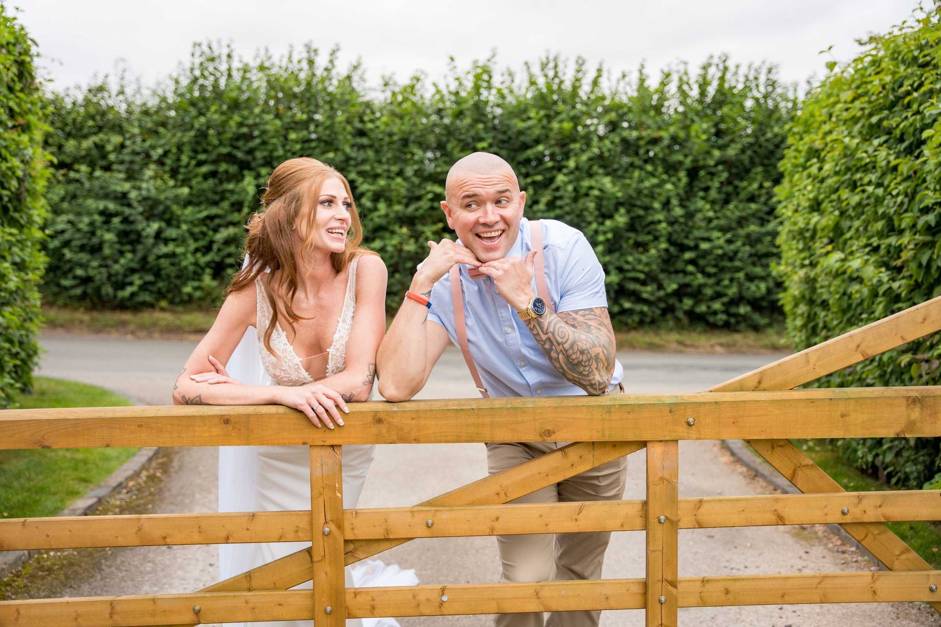 A bride and groom are leaning over a wooden fence.