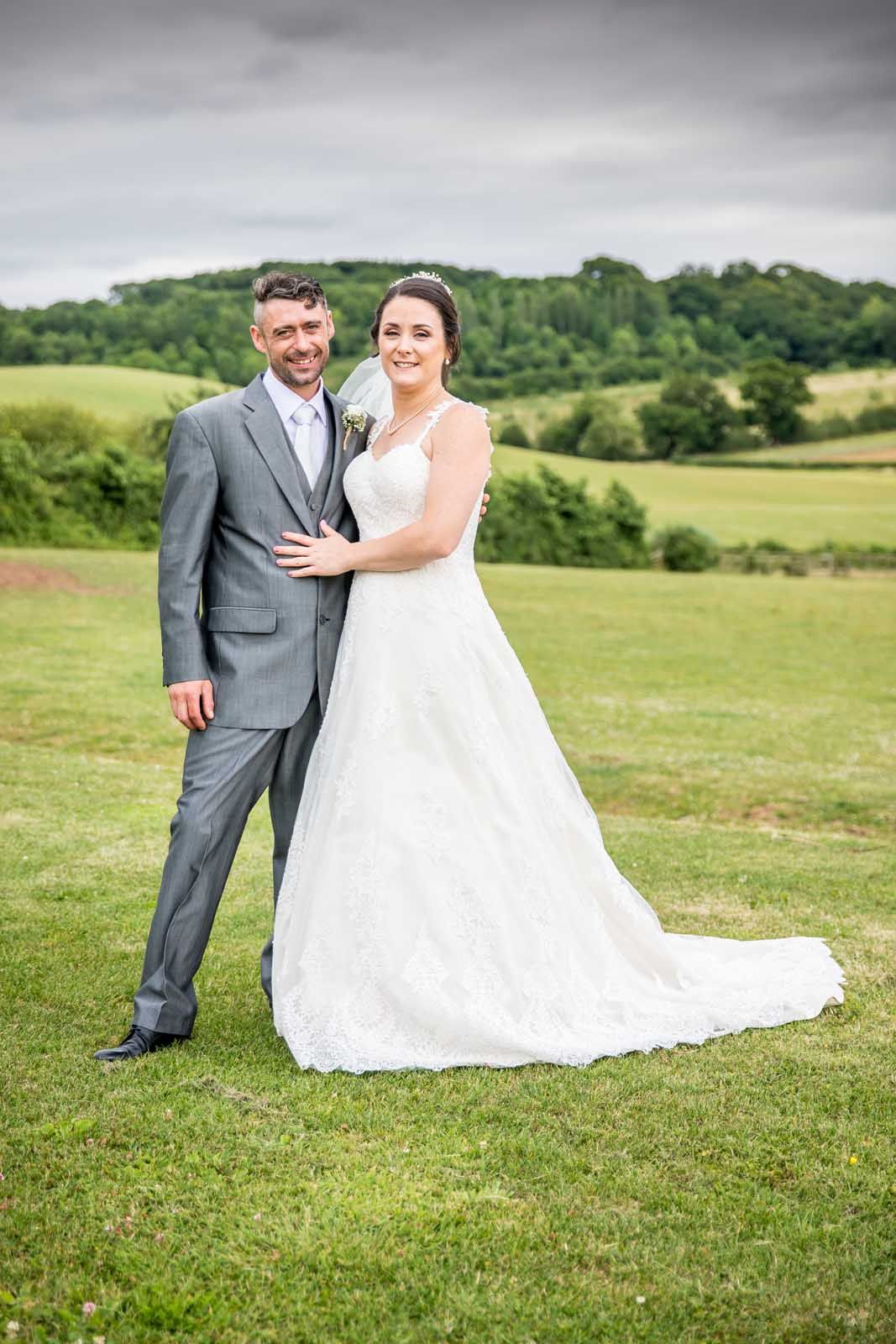A bride and groom are posing for a picture in a field.