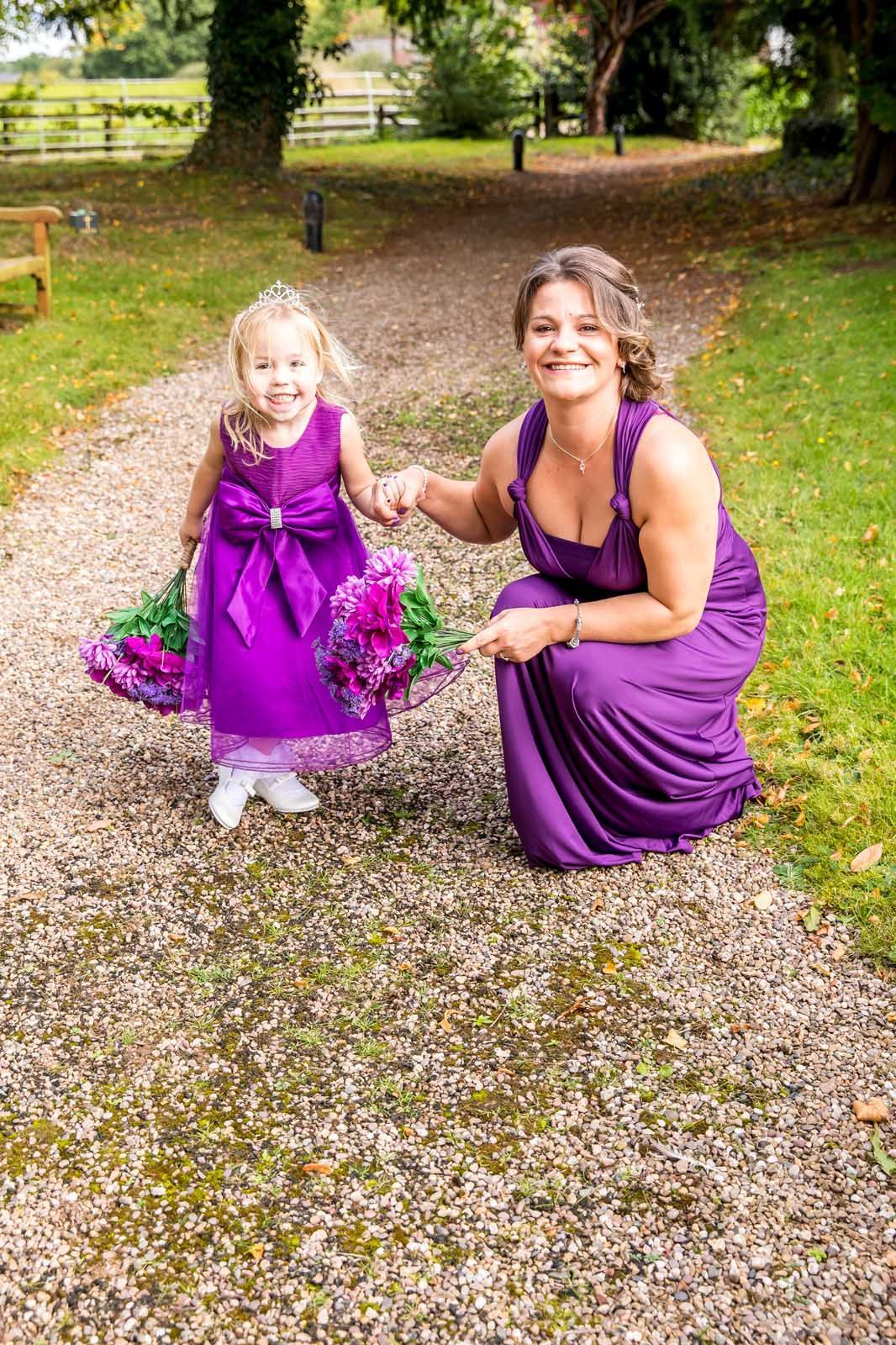 A woman in a purple dress is kneeling next to a flower girl in a purple dress.
