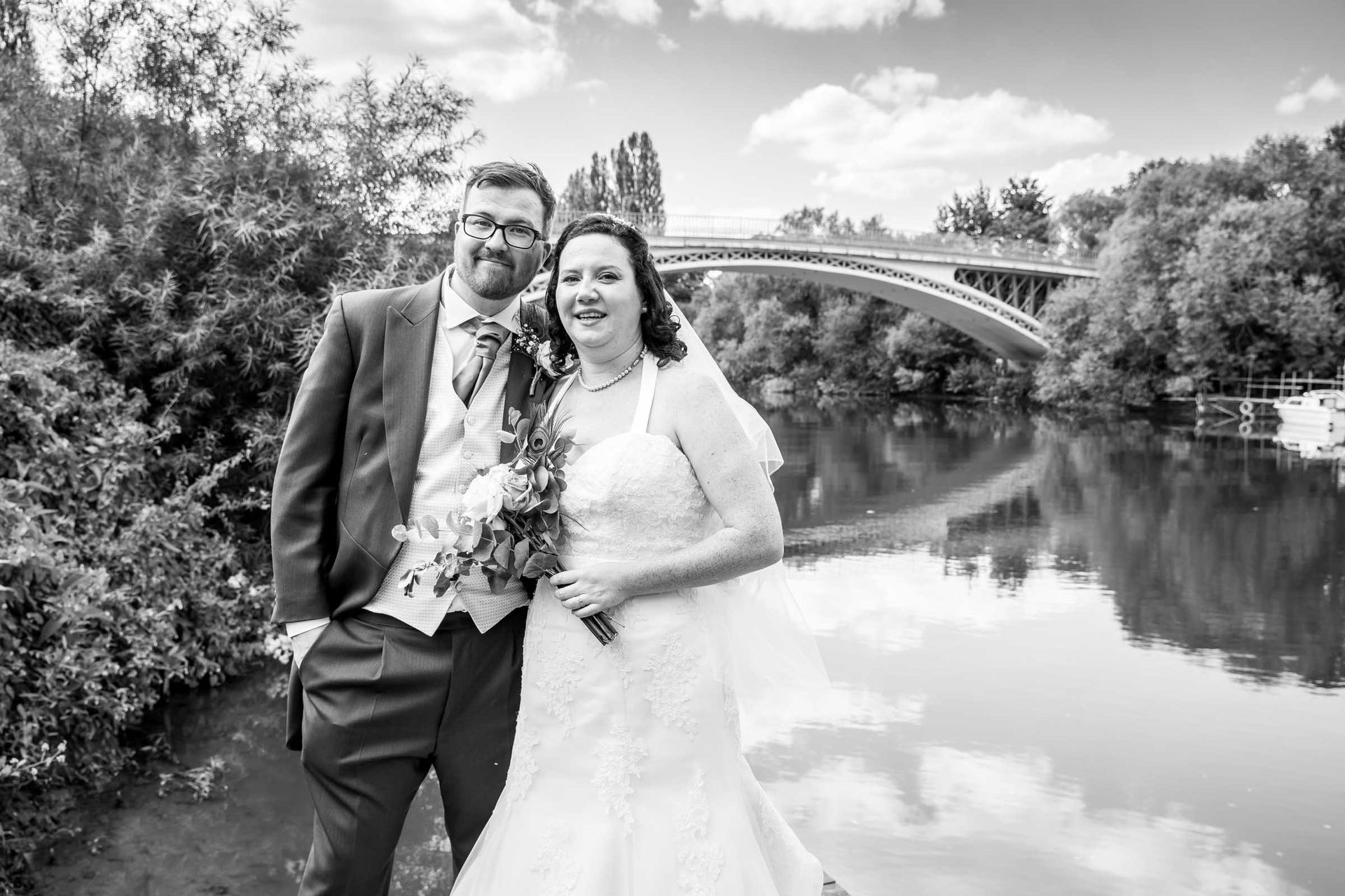 A black and white photo of a bride and groom standing next to a river.