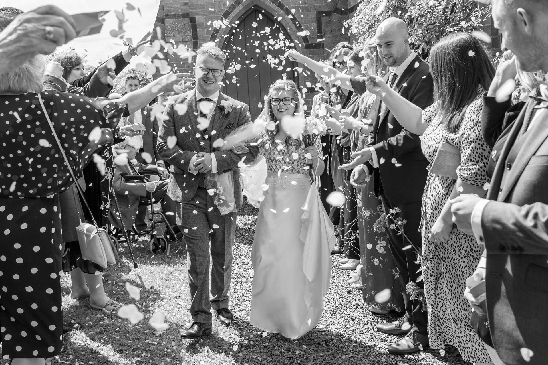 A bride and groom are walking through a crowd of people throwing confetti at them.