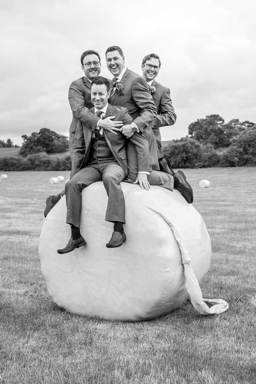 A group of men are sitting on top of a bale of hay.