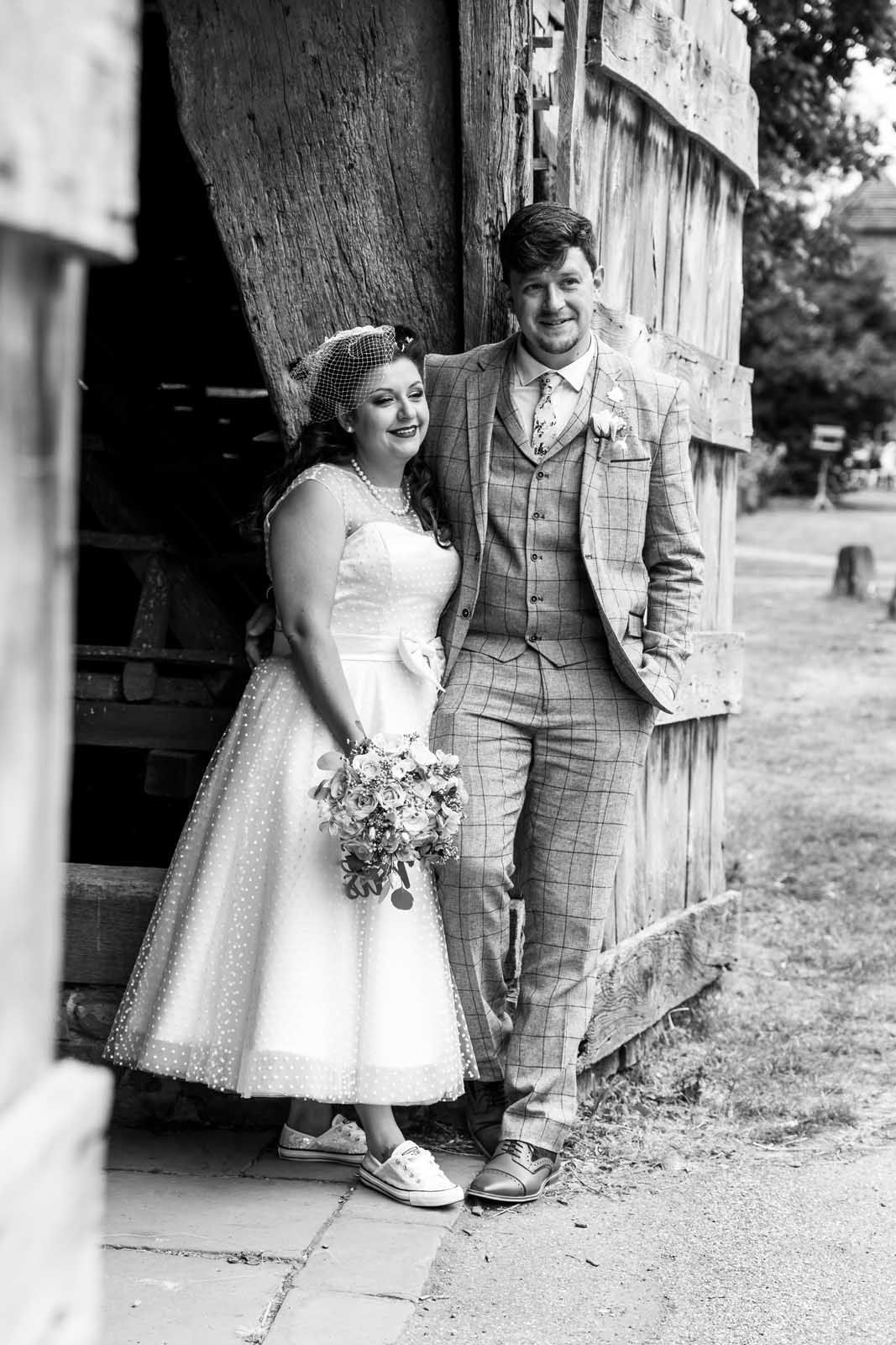 A bride and groom are posing for a black and white photo in front of a barn.