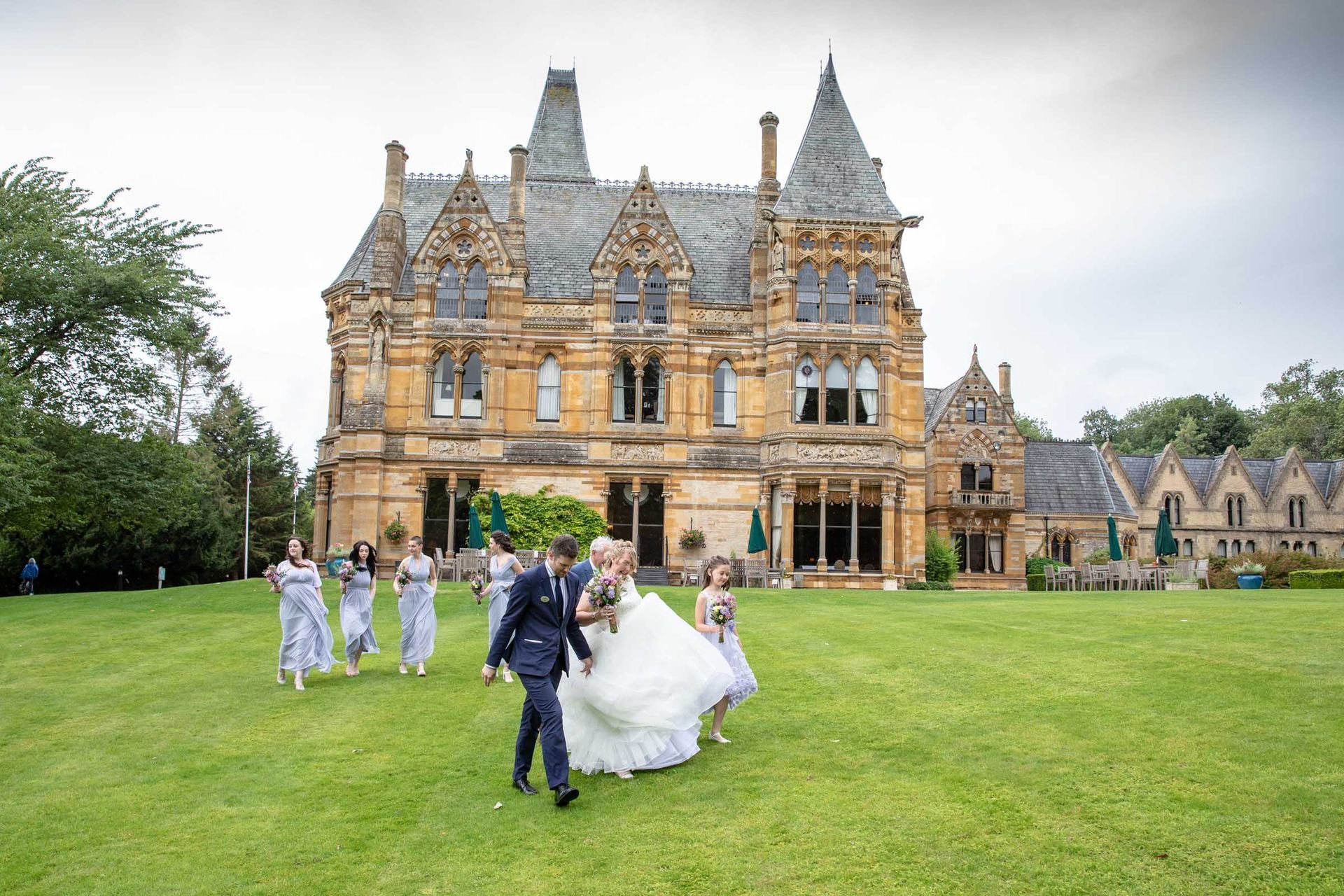 A bride and groom are walking with their wedding party in front of a large castle.