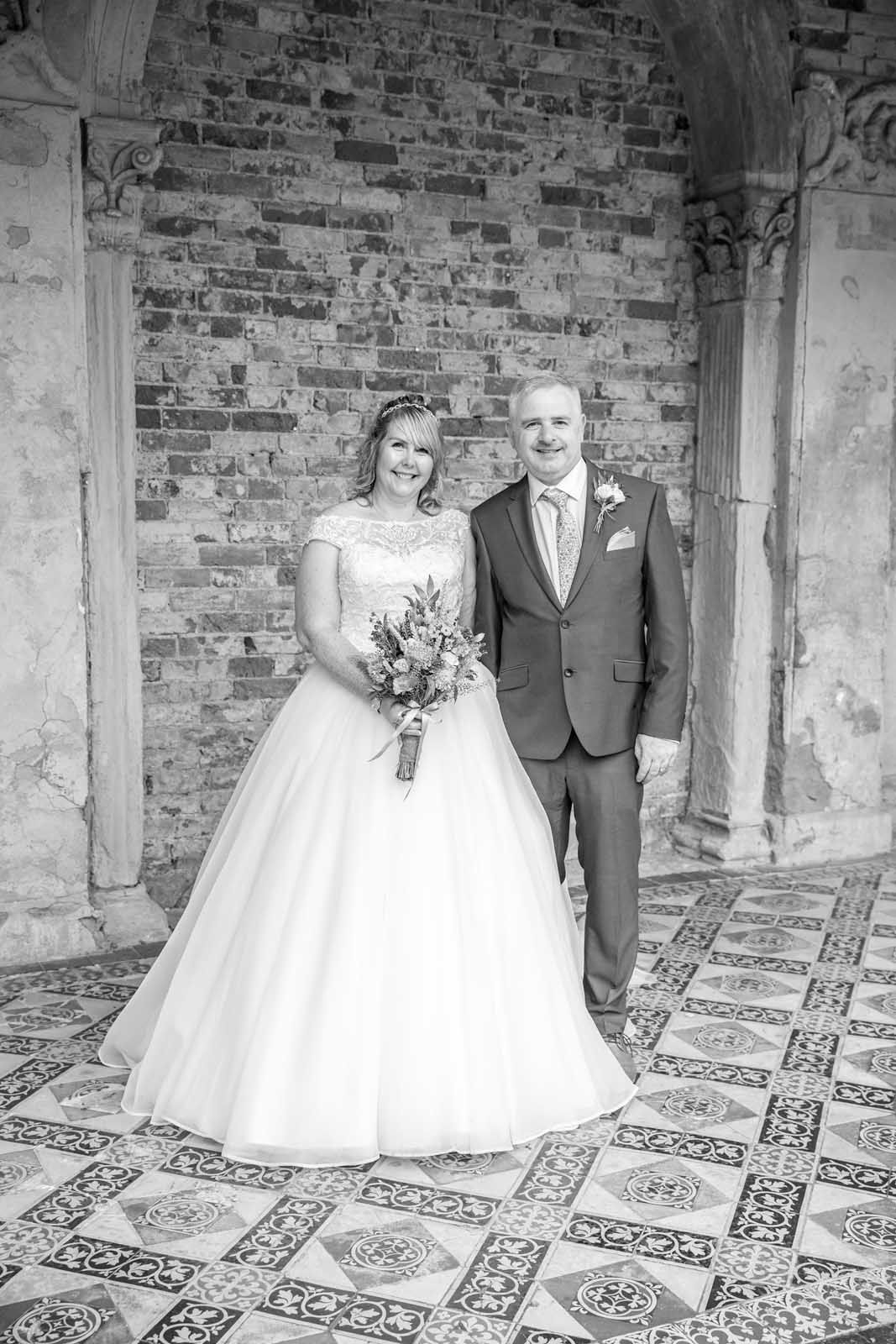 A bride and groom are posing for a black and white photo in front of a brick wall.