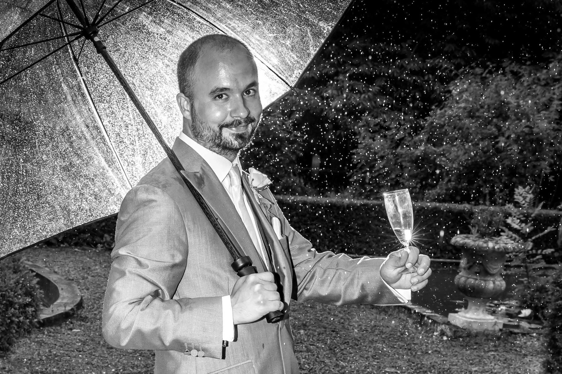 A man in a suit is holding an umbrella and a glass of champagne.