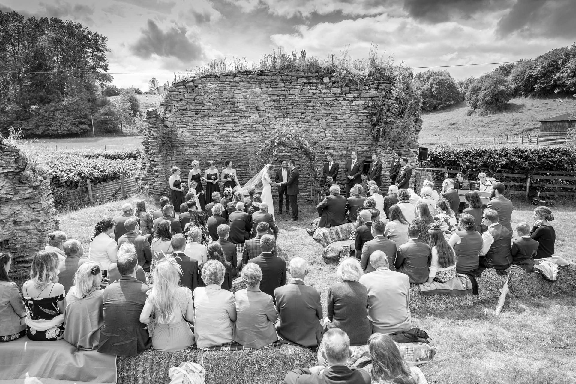 A black and white photo of a group of people sitting in front of a brick wall.