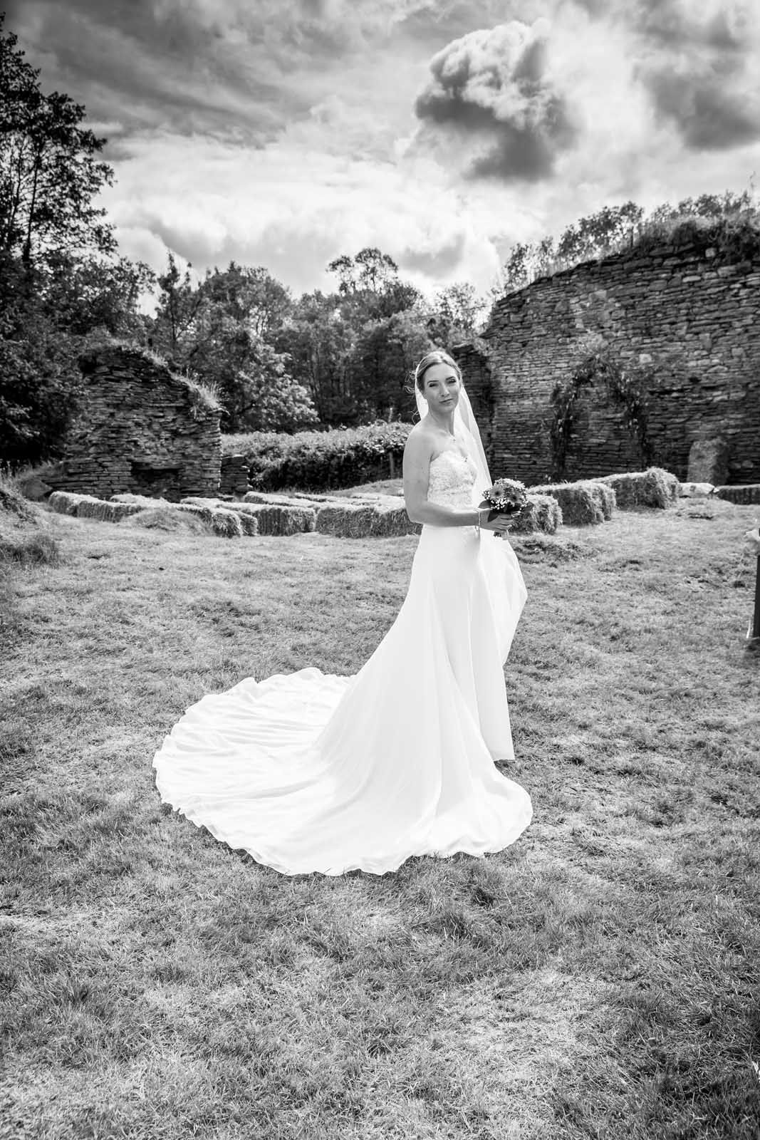 A black and white photo of a bride in a wedding dress standing in a field.