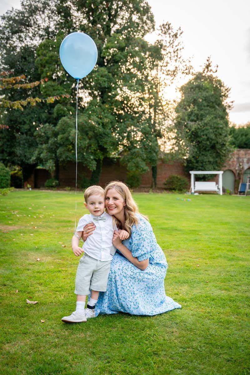 A woman is sitting on the grass with a baby and holding a blue balloon.