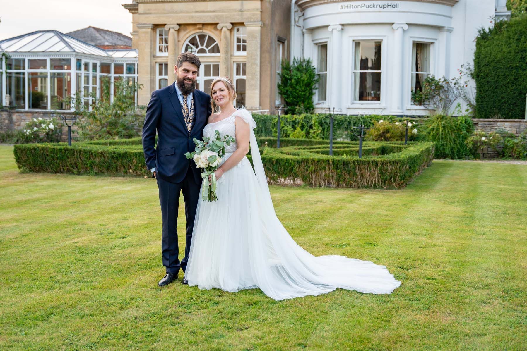A bride and groom are posing for a picture in front of a large house.