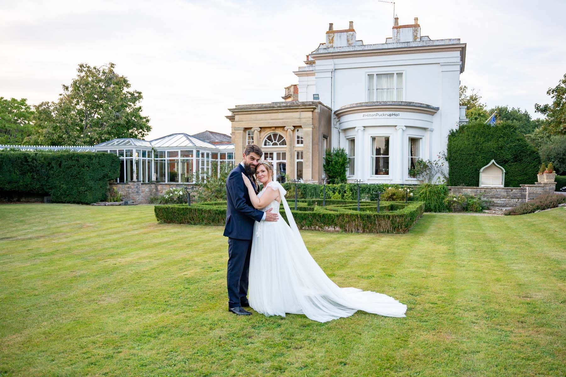 A bride and groom are posing for a picture in front of a large white house.