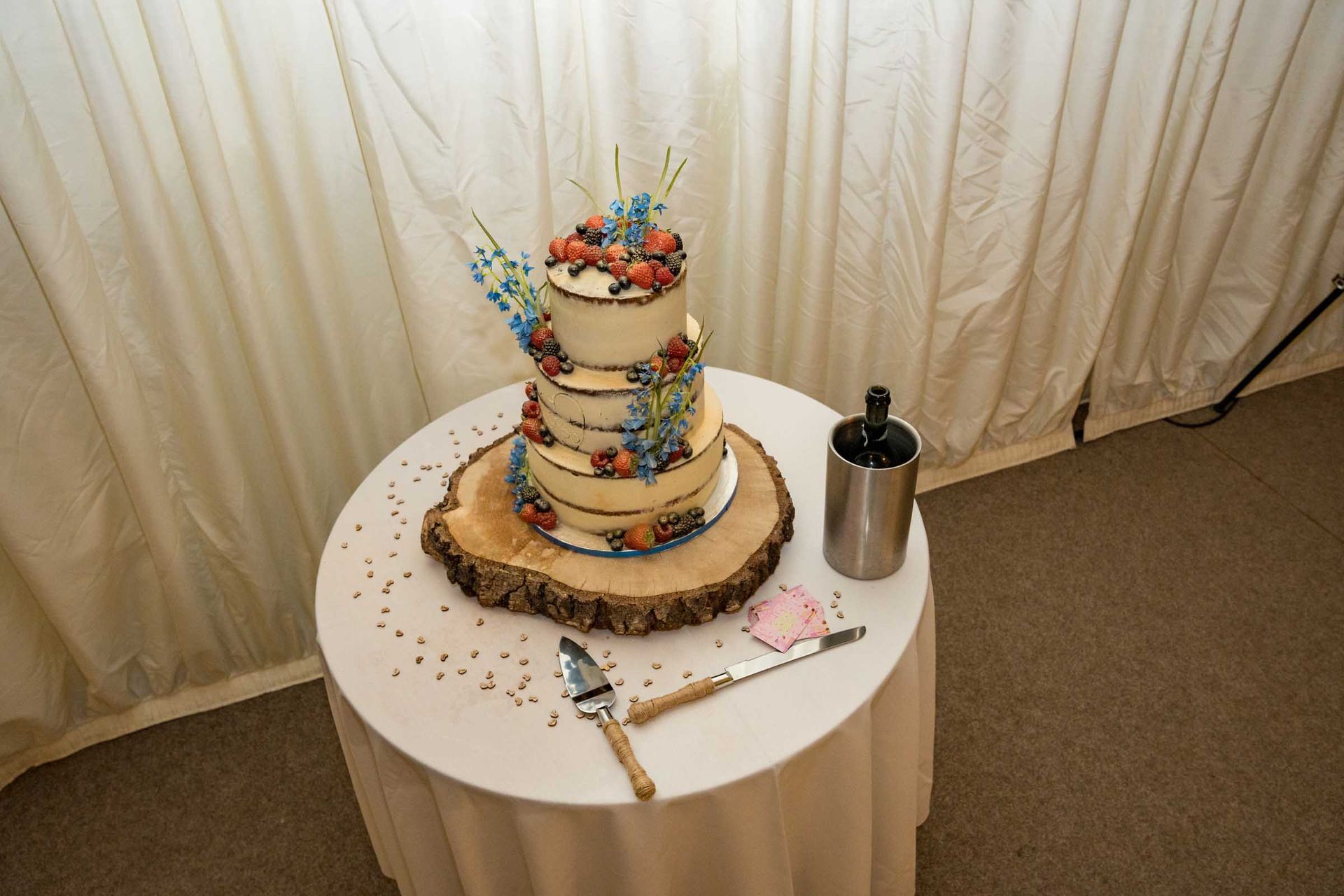 A wedding cake is sitting on a wooden slice on a table.