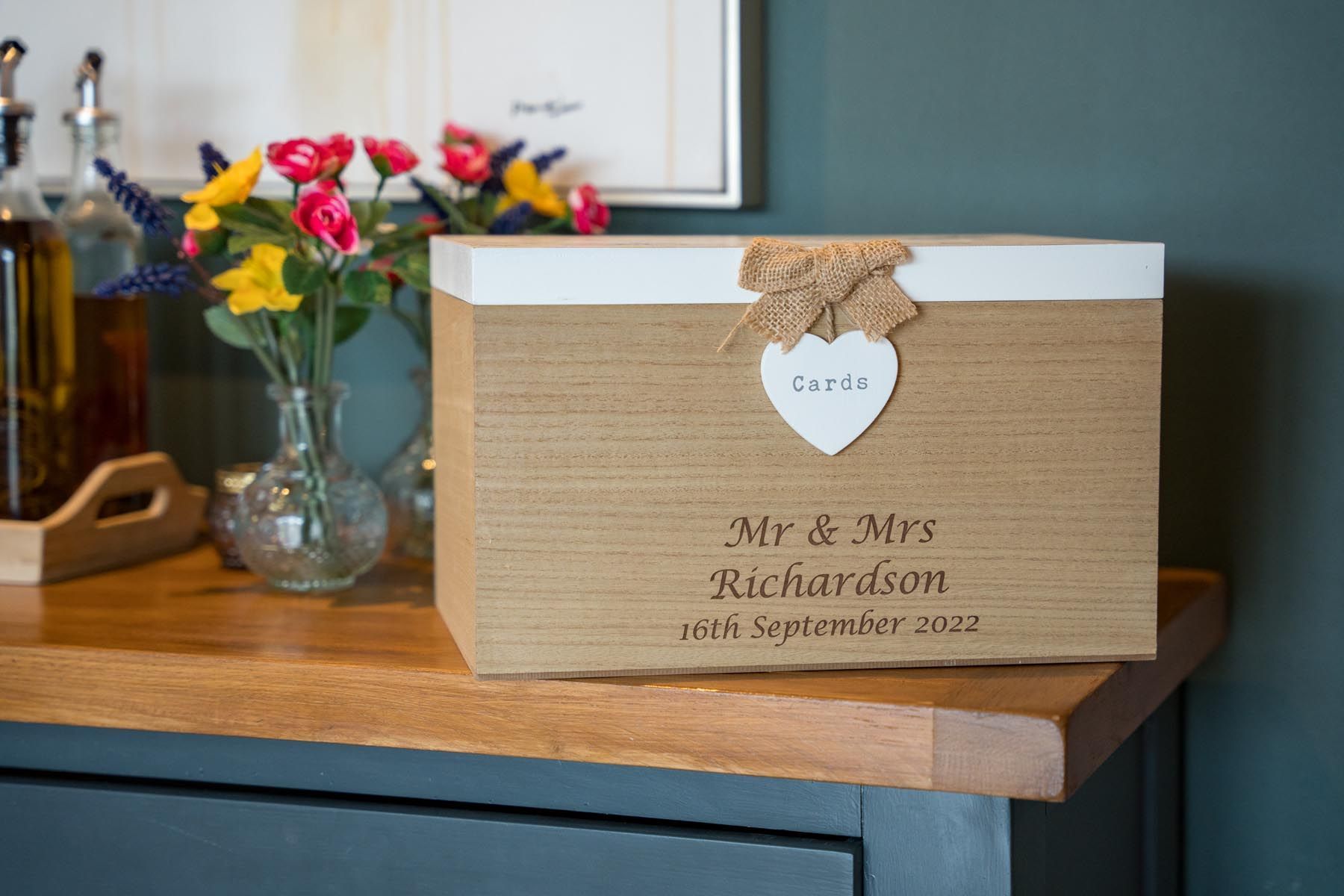 A card box is sitting on a wooden table next to a vase of flowers.
