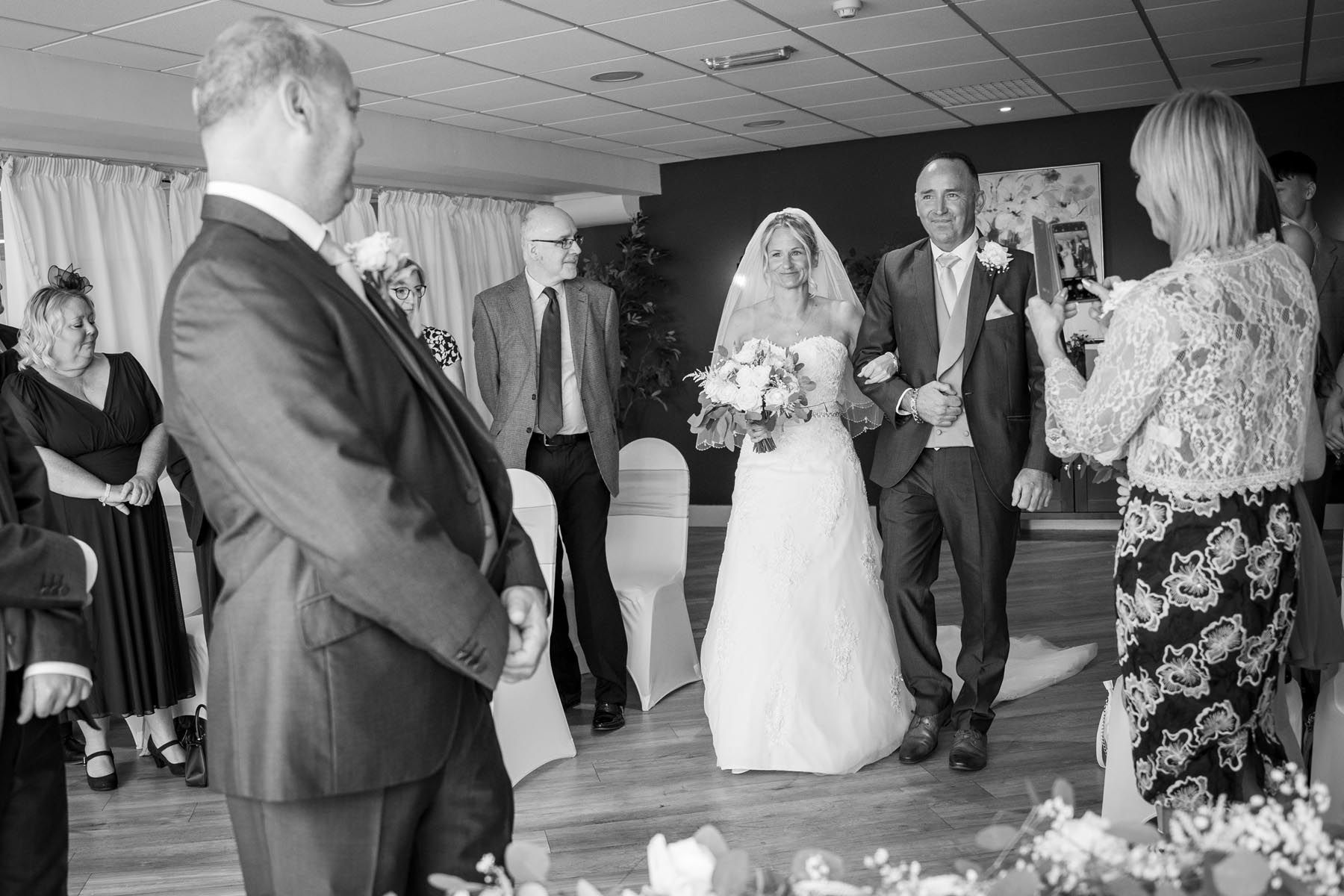 A black and white photo of a bride and groom walking down the aisle at a wedding.