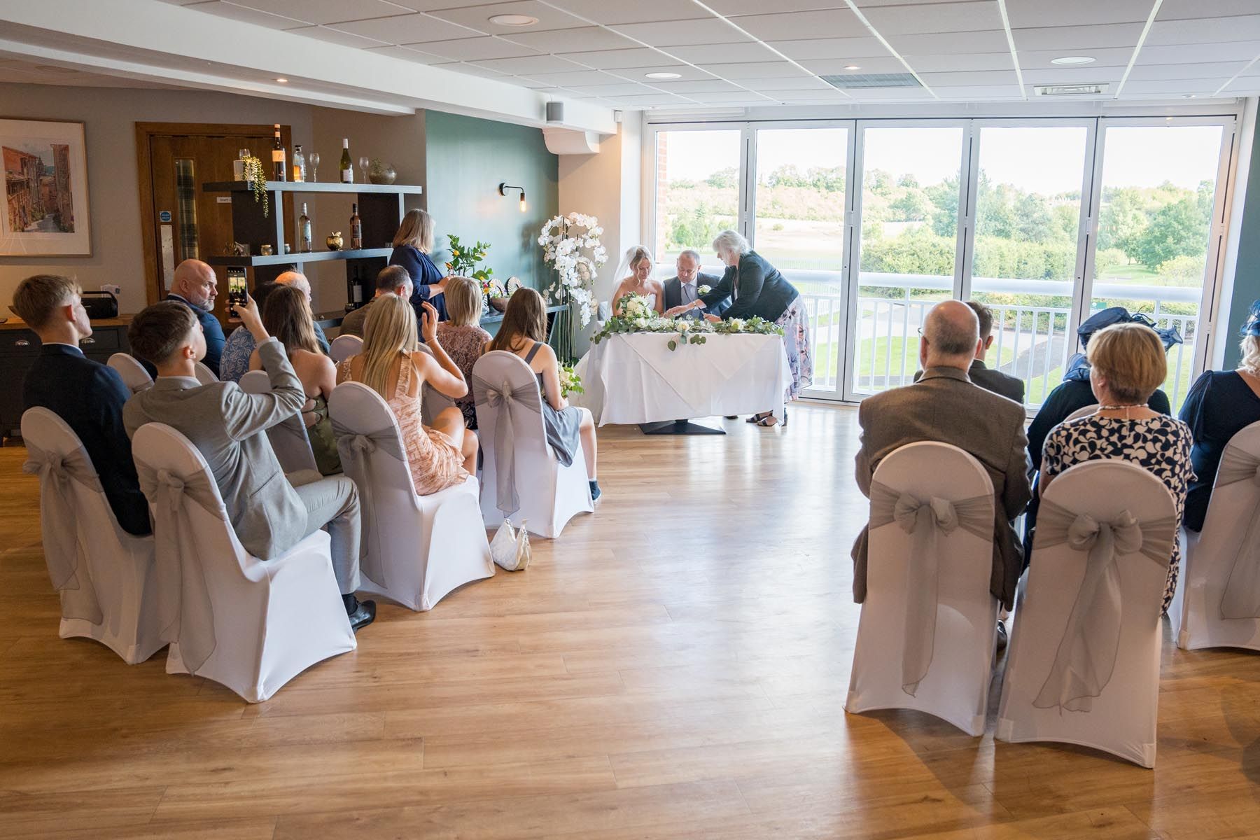 A group of people are sitting in chairs in front of a table at a wedding ceremony.