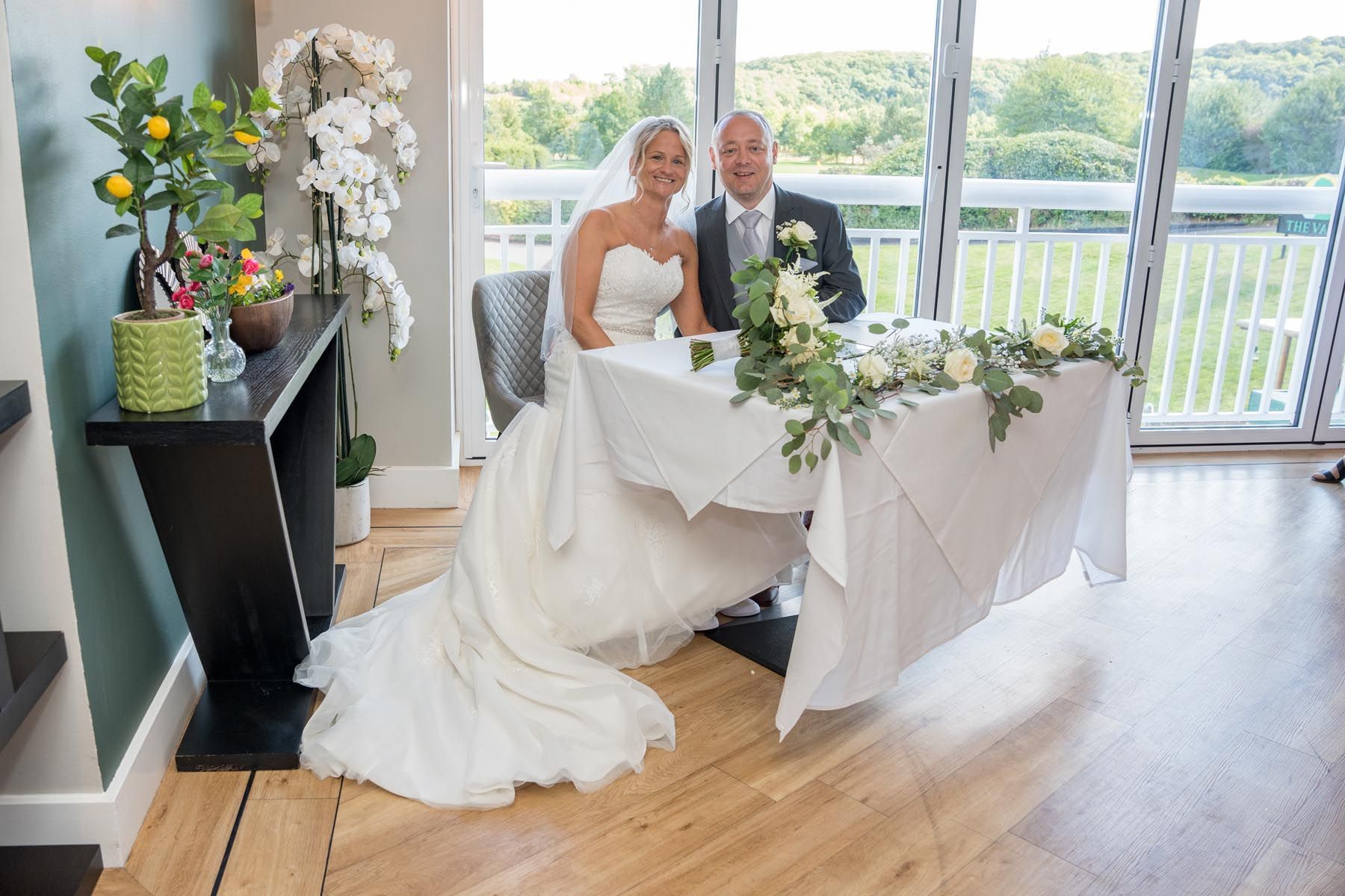 A bride and groom are sitting at a table in front of a window.