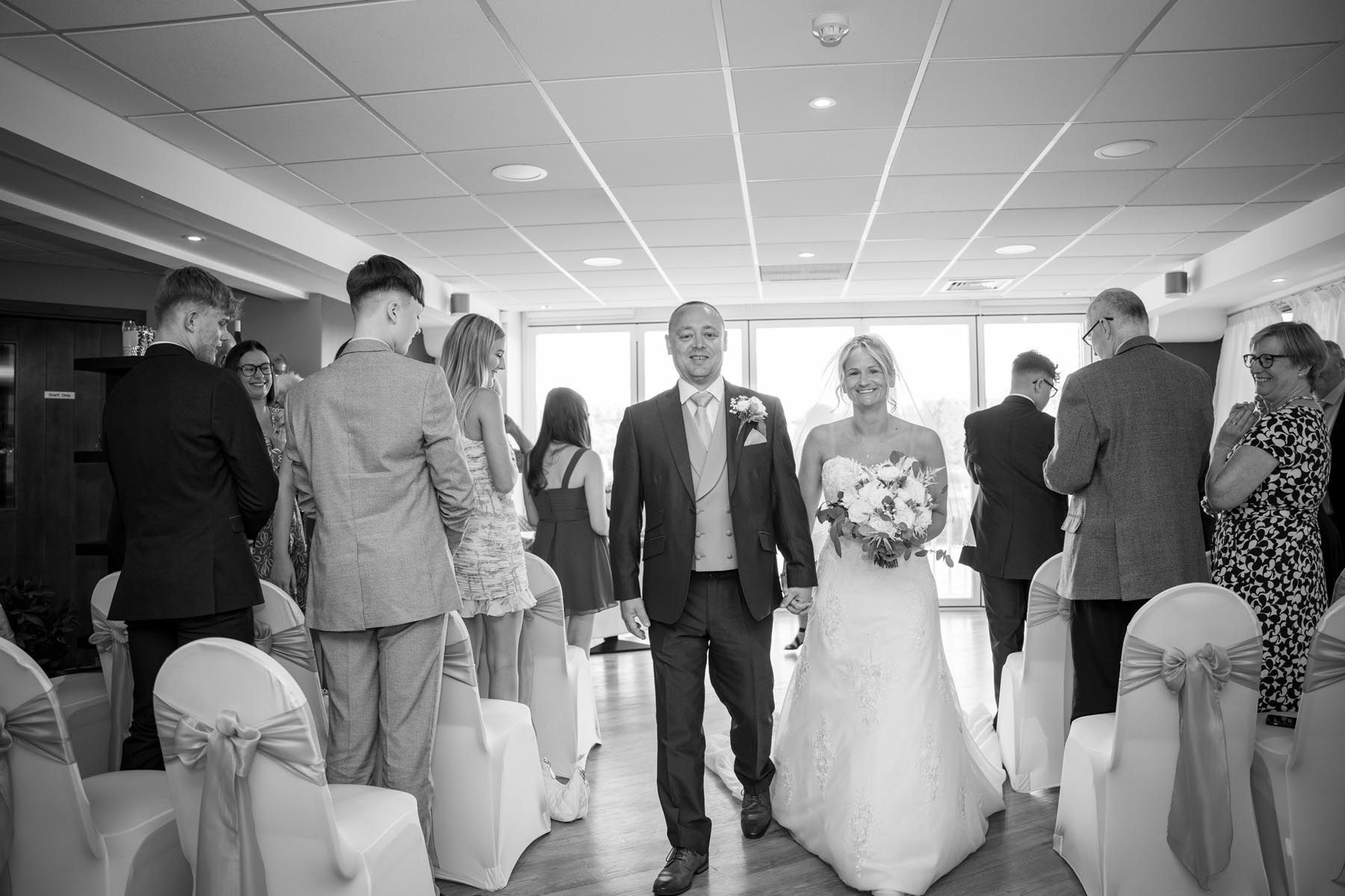 A black and white photo of a bride and groom walking down the aisle at their wedding.