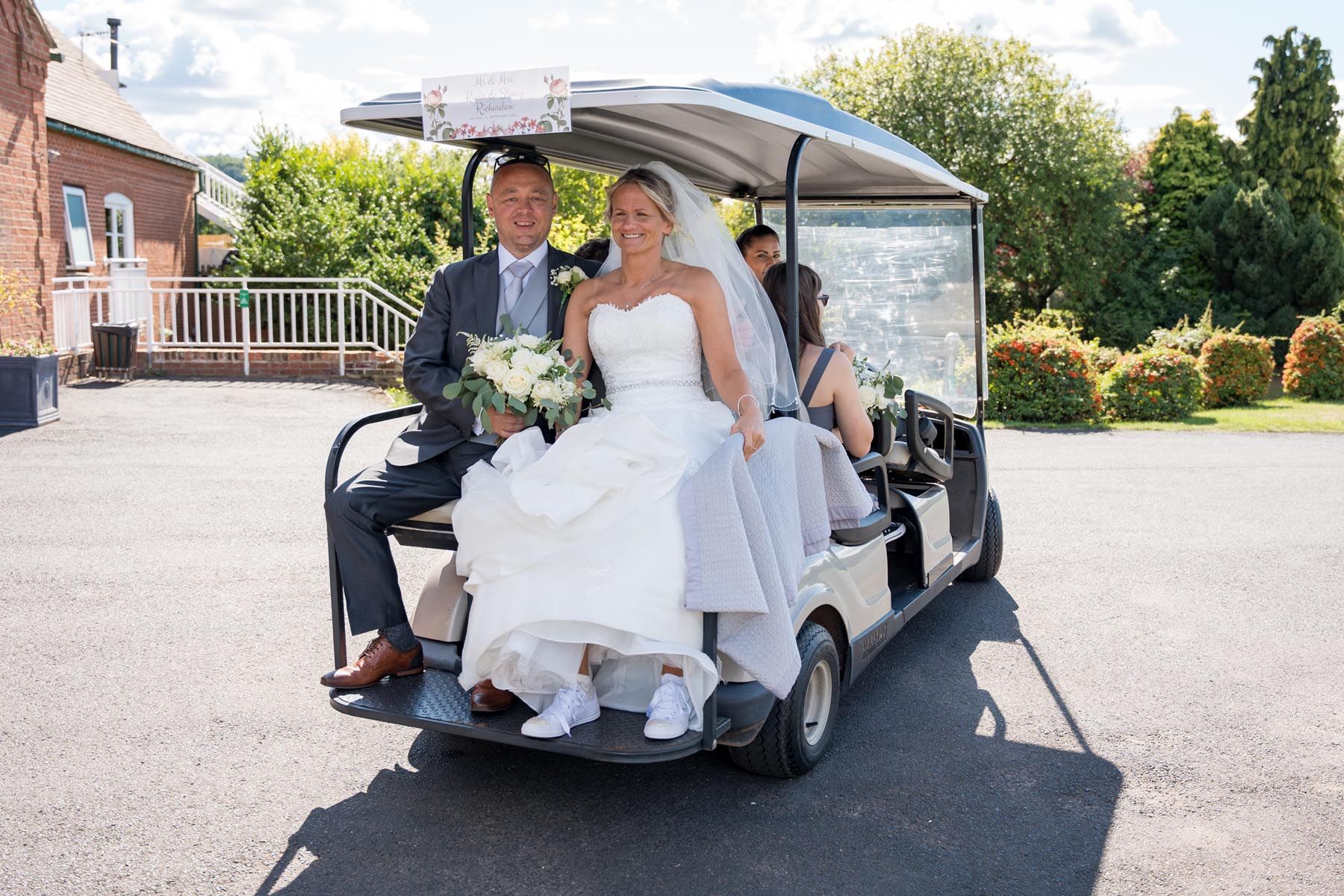 A bride and groom are sitting on the back of a golf cart.