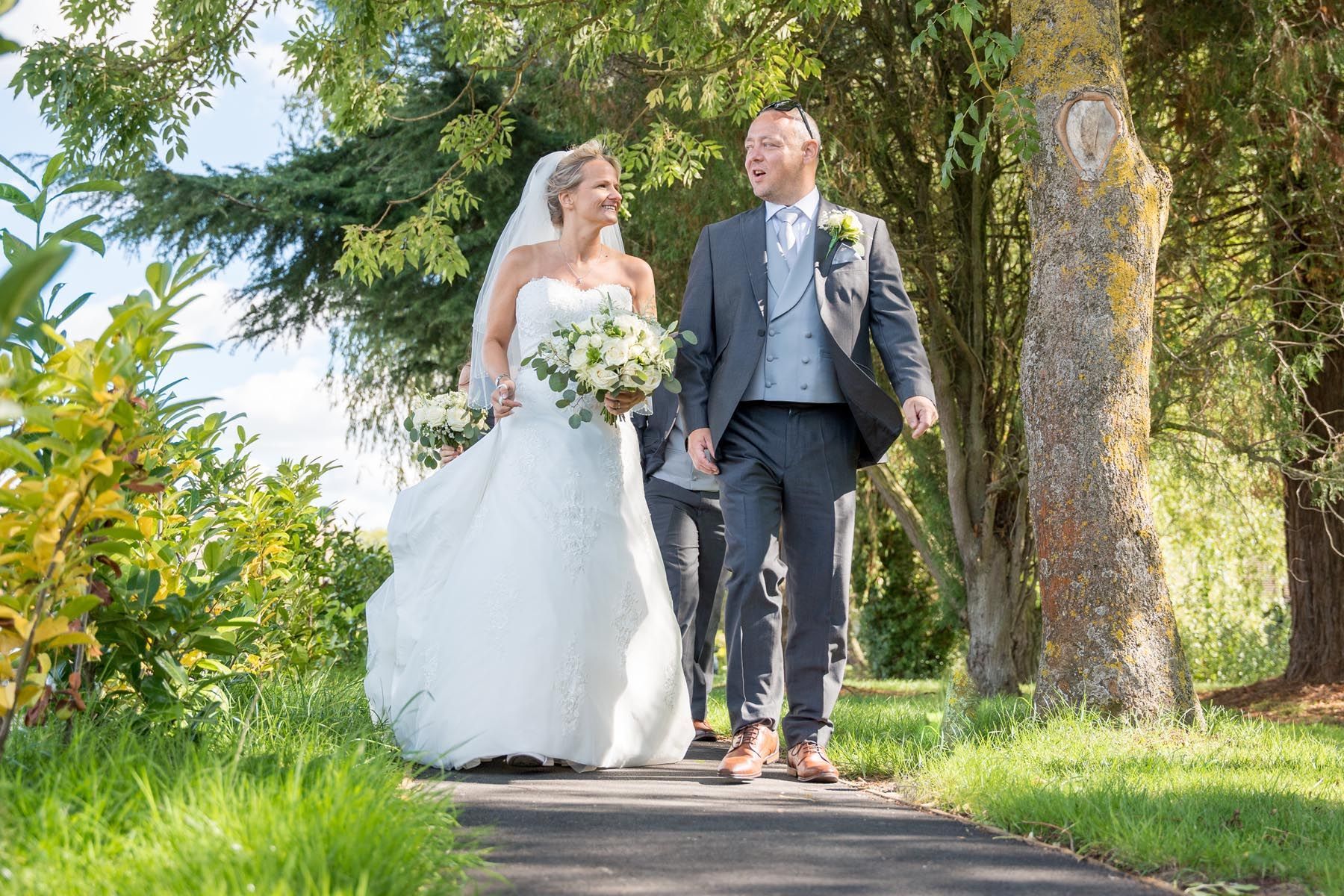 A bride and groom are walking down a path holding hands.