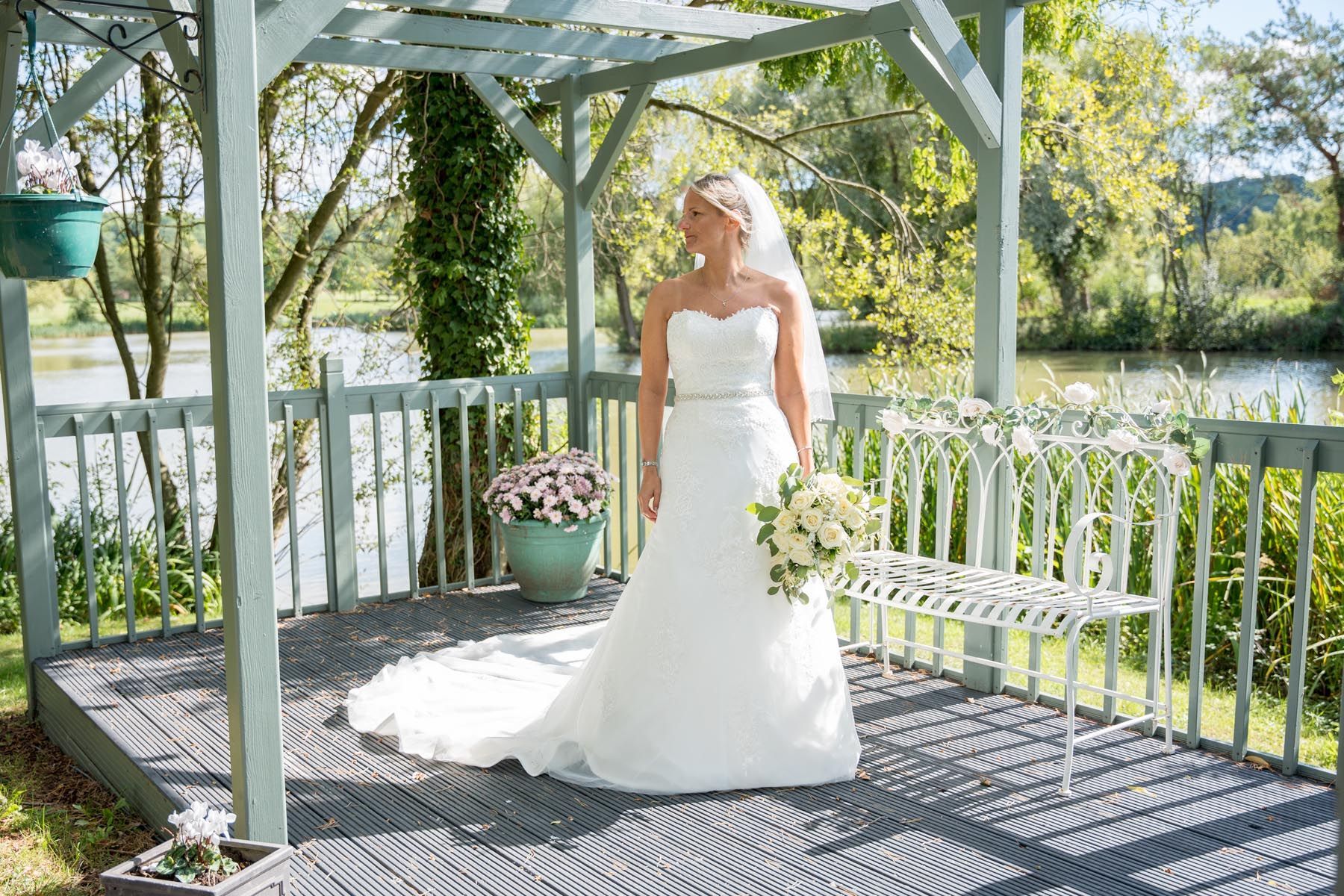 A bride in a wedding dress is standing under a pergola holding a bouquet of flowers.