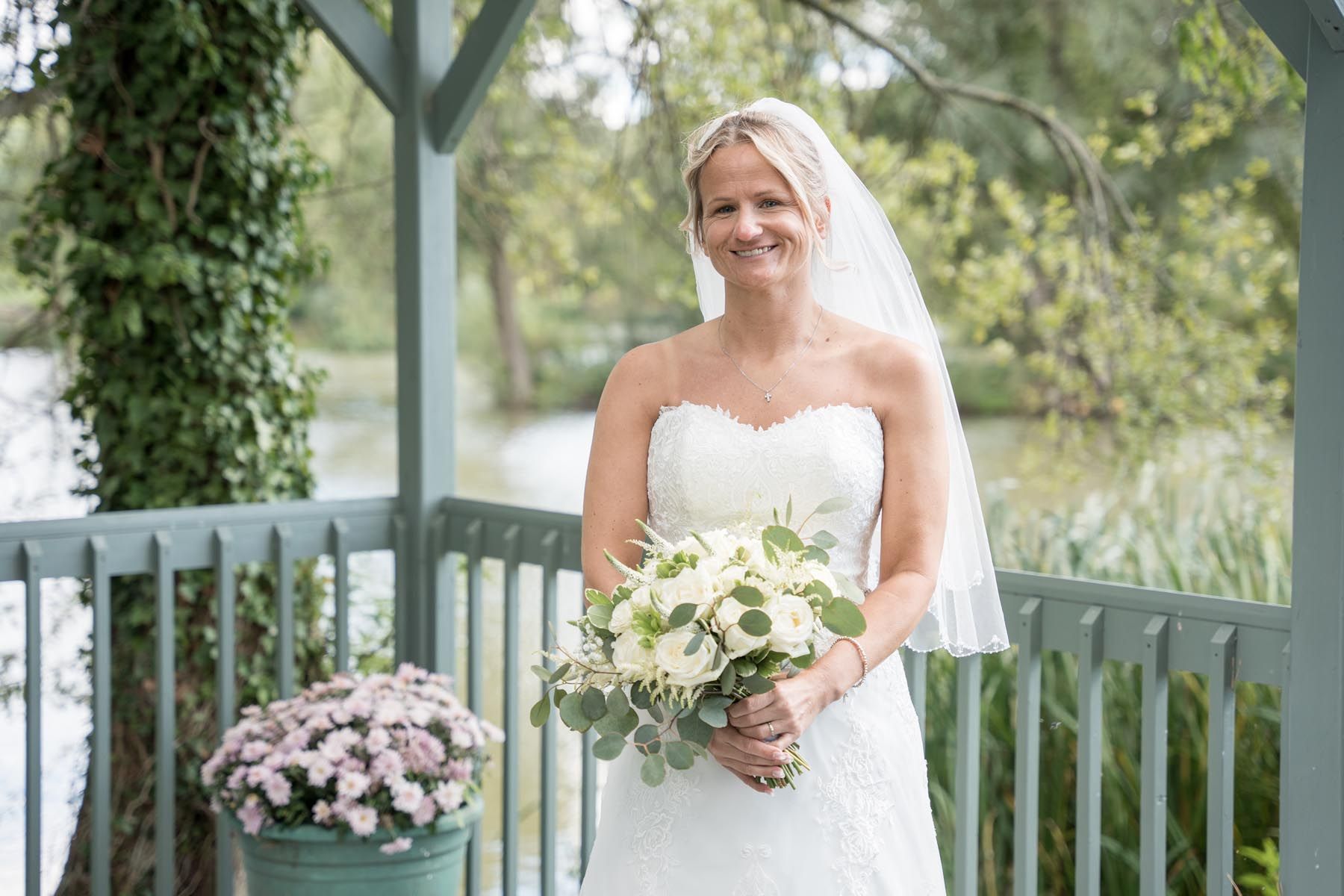 A bride in a wedding dress is standing on a balcony holding a bouquet of flowers.