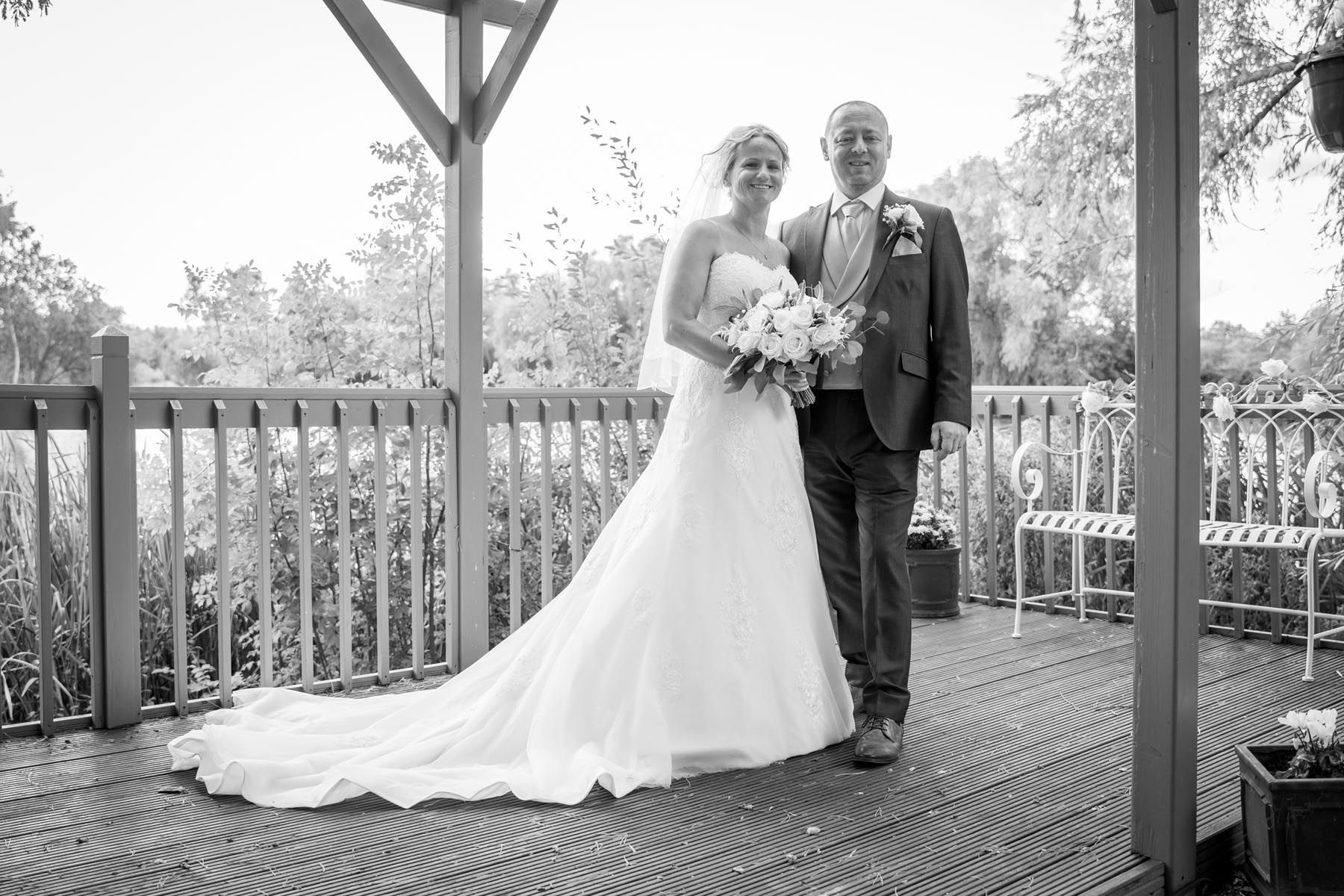 A bride and groom are posing for a black and white photo on a deck.