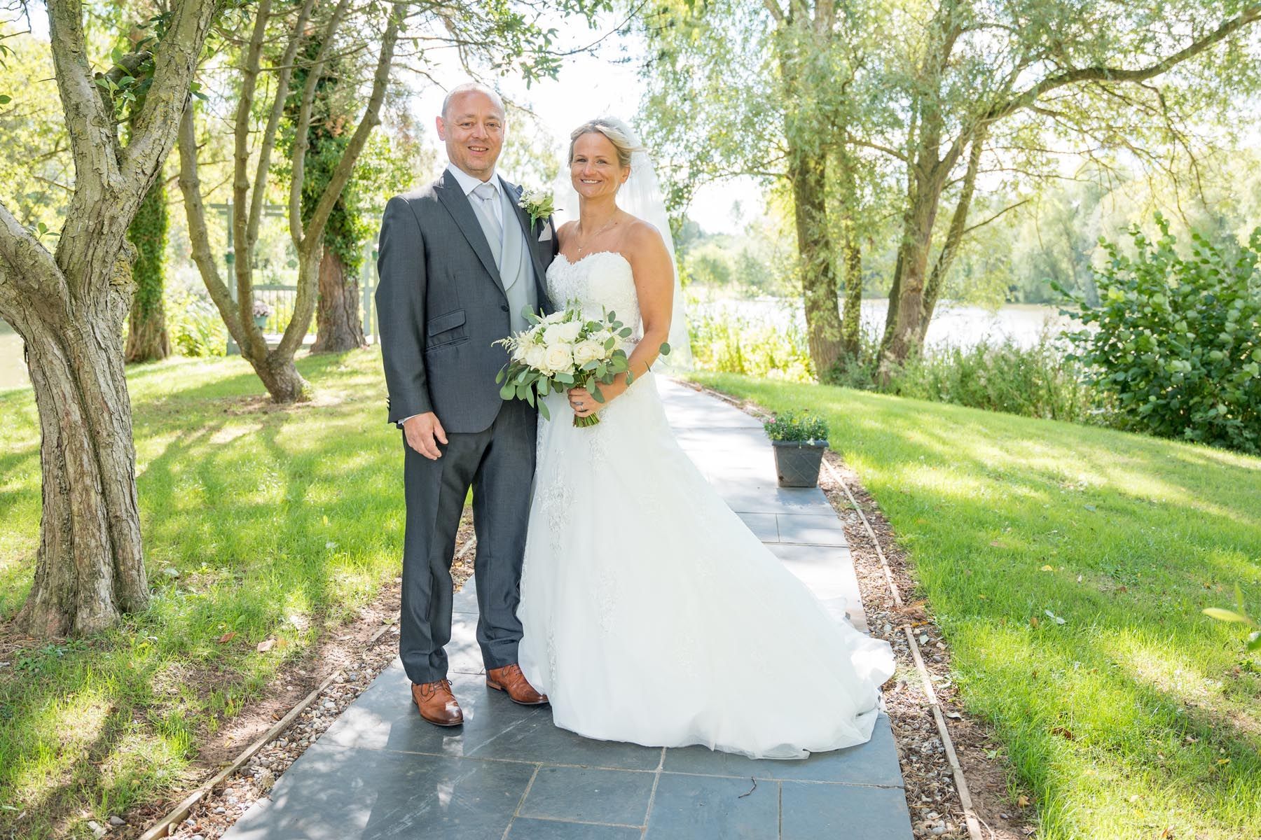 A bride and groom are posing for a picture on a path in the woods.