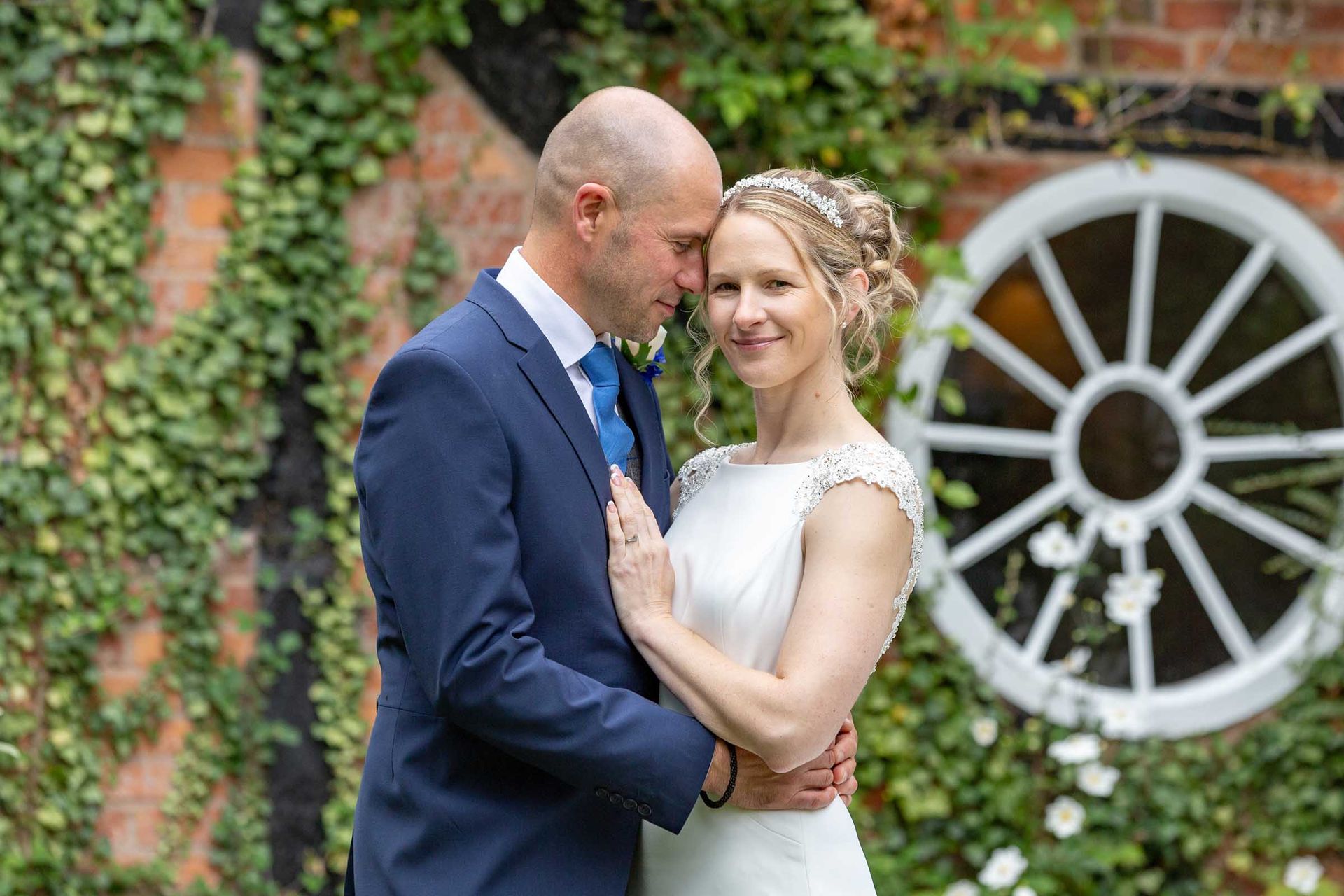 A bride and groom are posing for a picture in front of a wagon wheel.