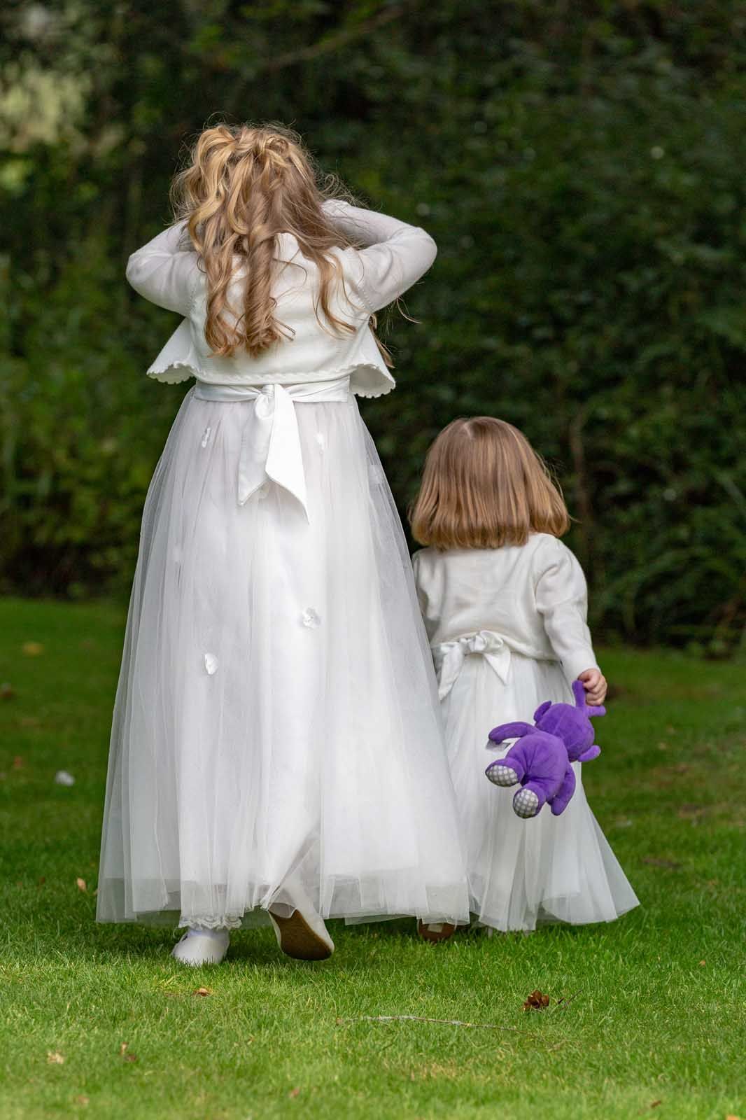 A flower girl and a bridesmaid are walking in the grass holding hands.