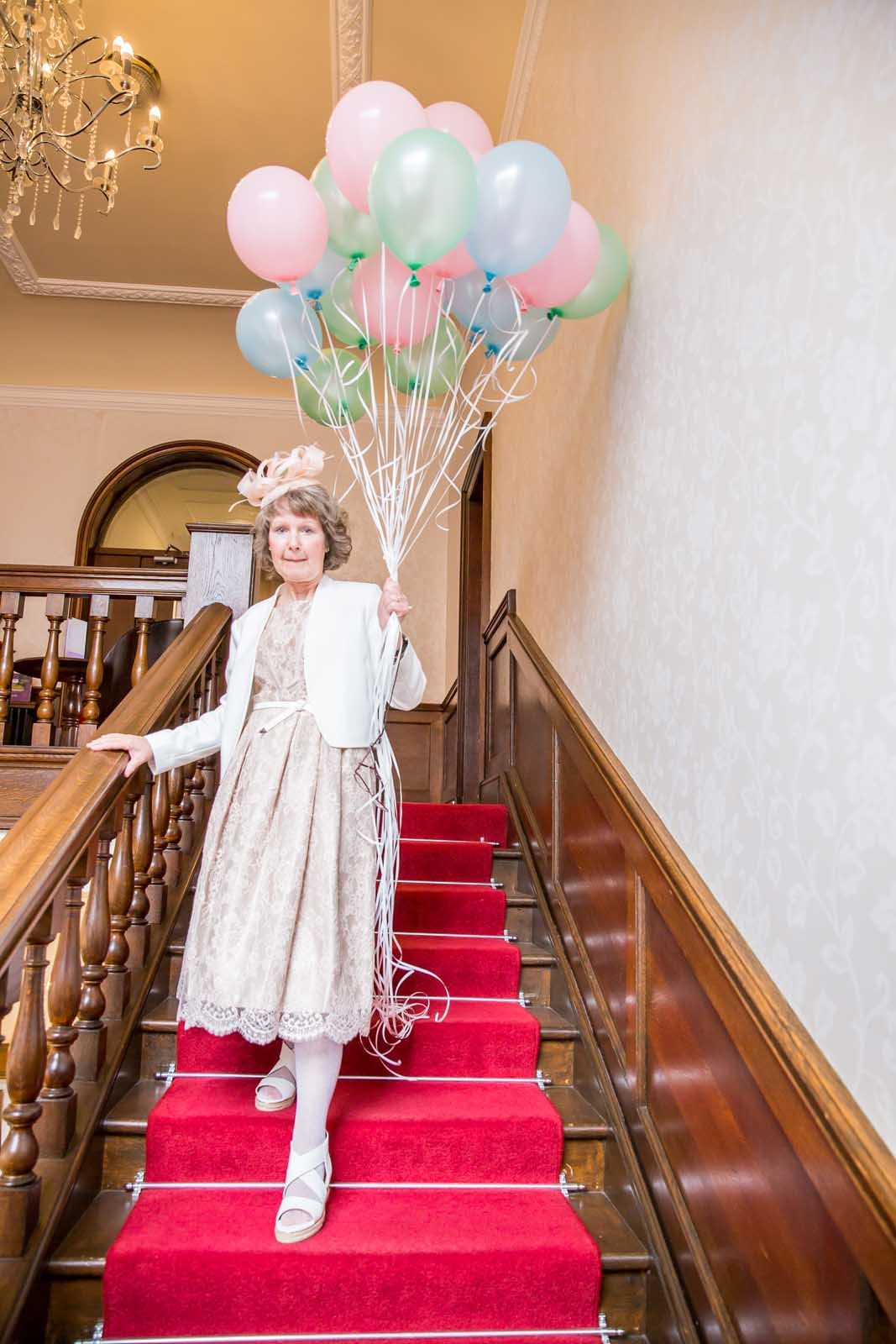 A woman is standing on a set of red stairs holding a bunch of balloons.