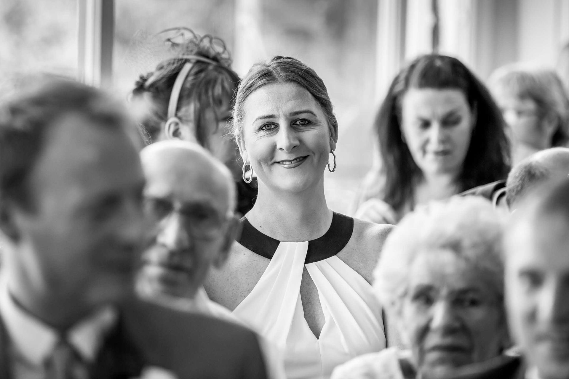A woman is smiling in a crowd of people at a wedding.