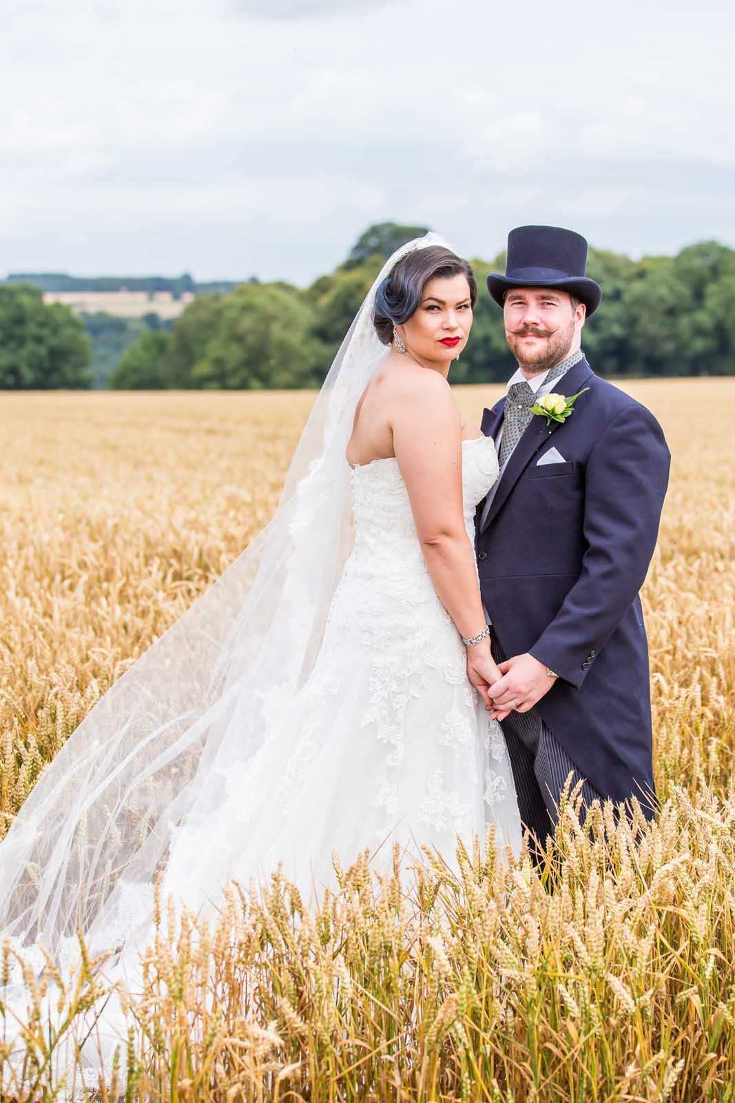 A bride and groom are posing for a picture in a field of wheat.