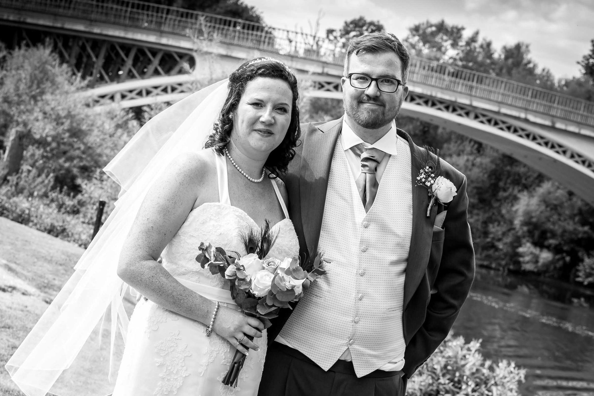A bride and groom are posing for a picture in front of a bridge.