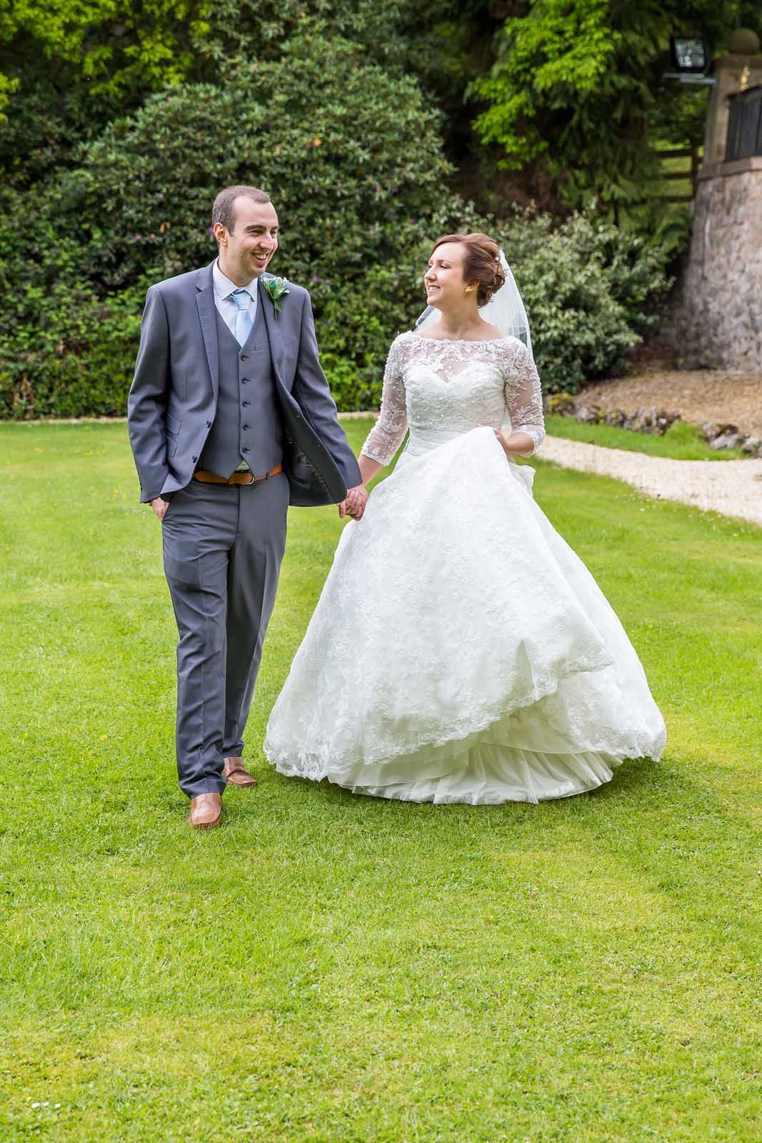 A bride and groom are walking through a grassy field holding hands.