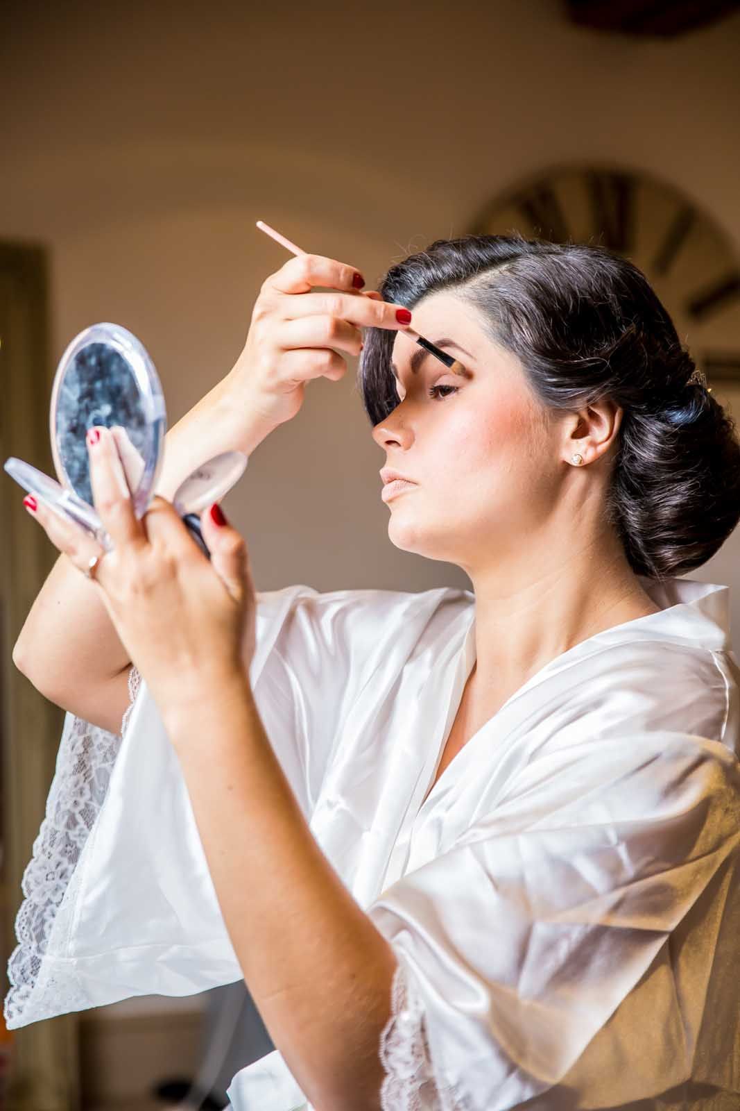 A woman is applying makeup to her eyebrows while looking in a mirror.