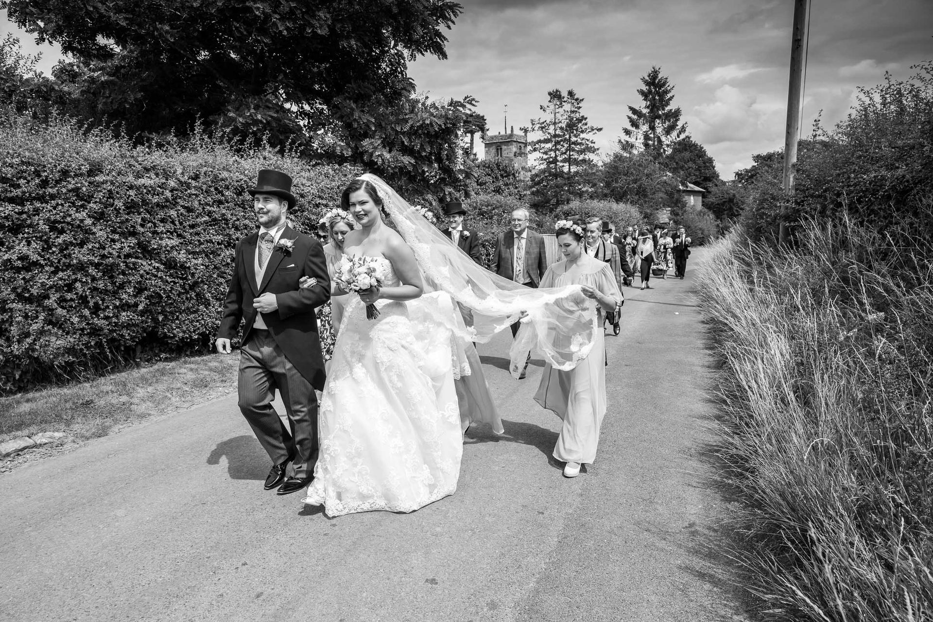 A bride and groom are walking down a road with their wedding party.