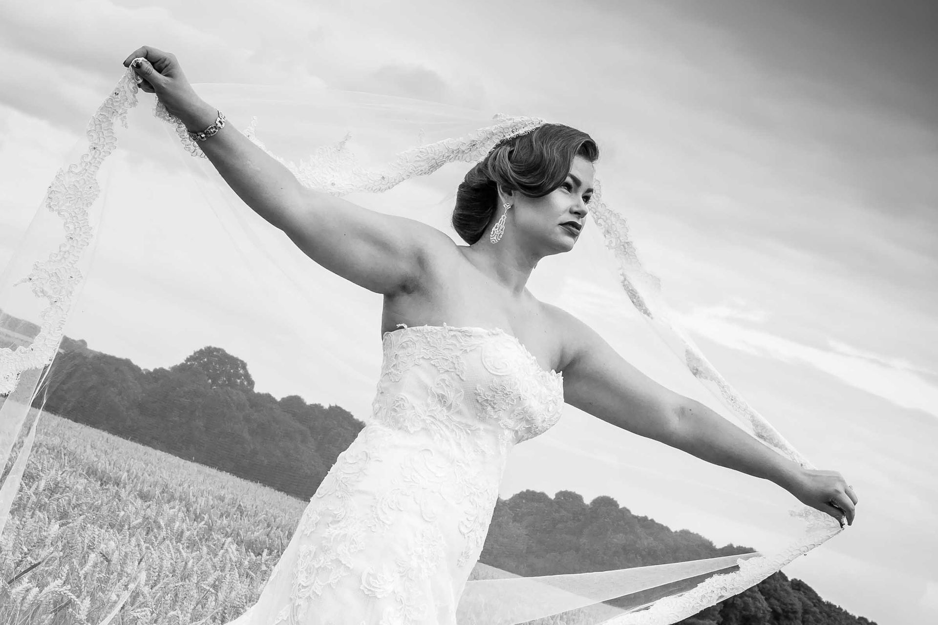 A black and white photo of a bride in a wedding dress holding a veil.