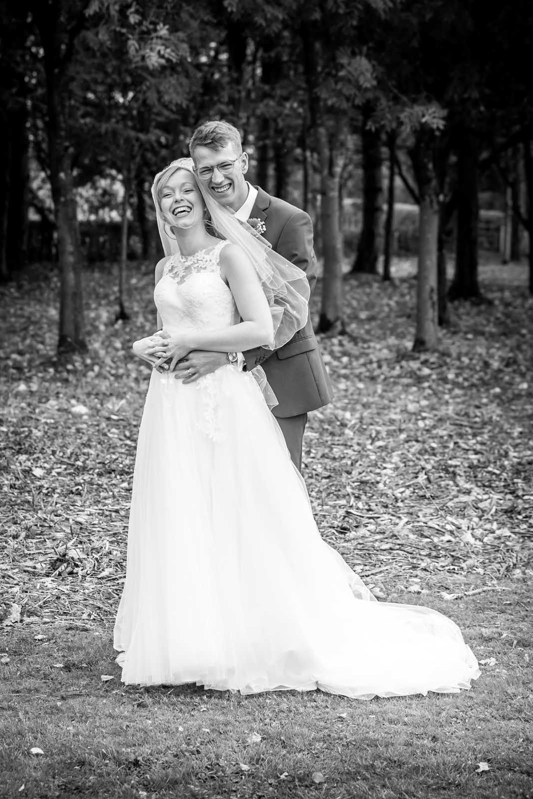 A bride and groom are posing for a black and white photo in the woods.