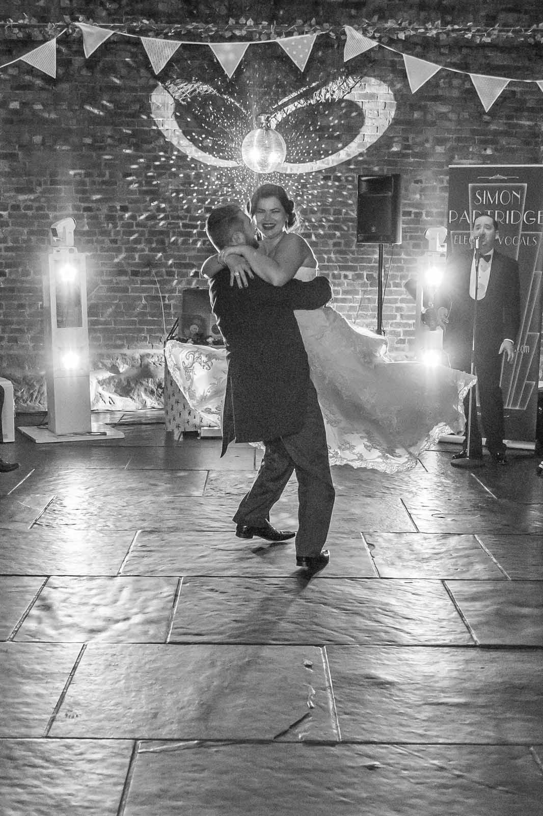 A bride and groom are dancing at their wedding reception in a black and white photo.