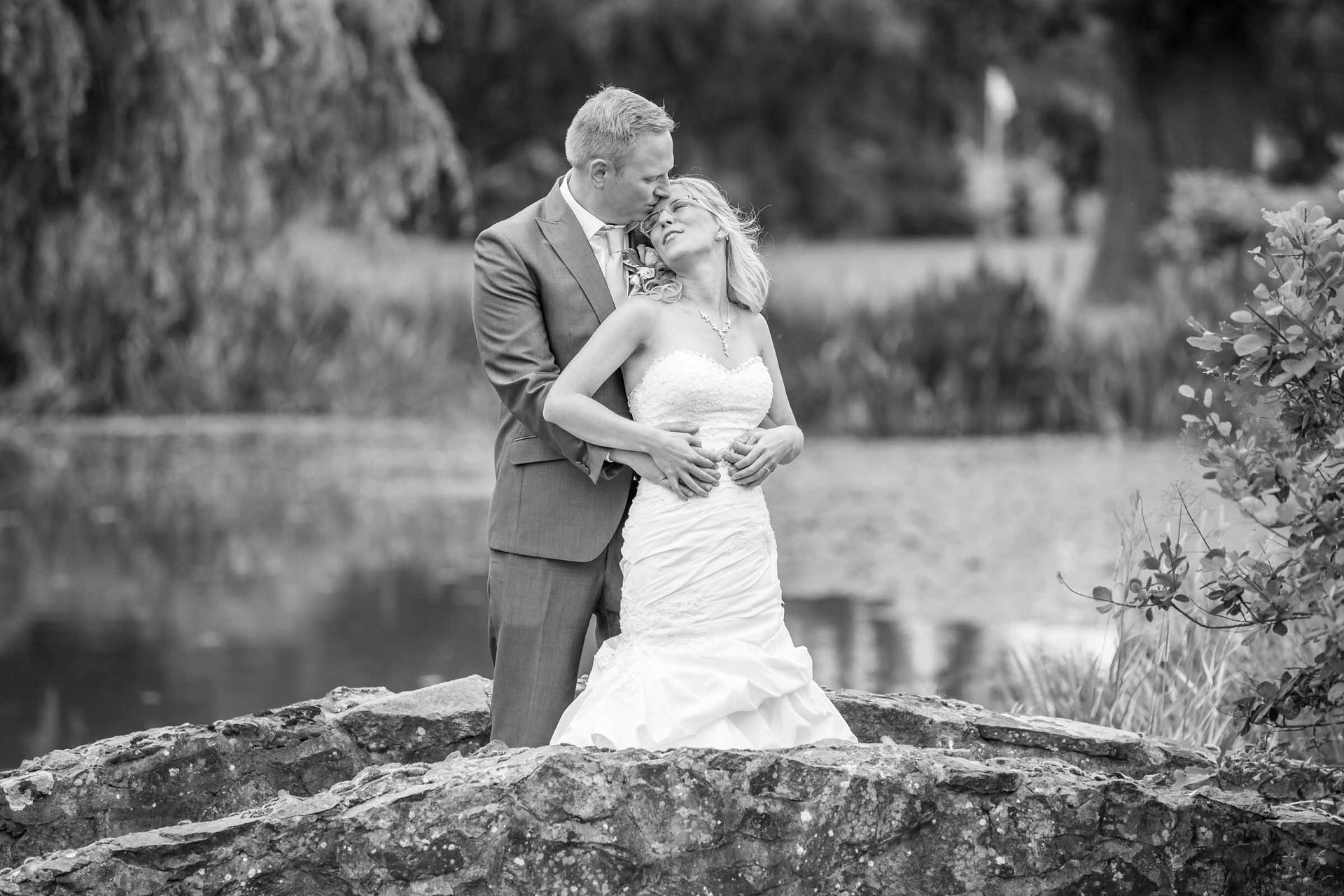 A bride and groom are kissing on a bridge in a black and white photo.