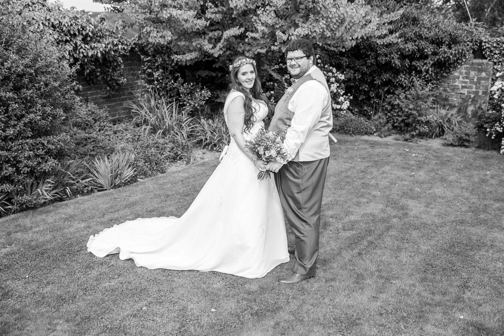 A bride and groom are posing for a black and white photo in the grass.