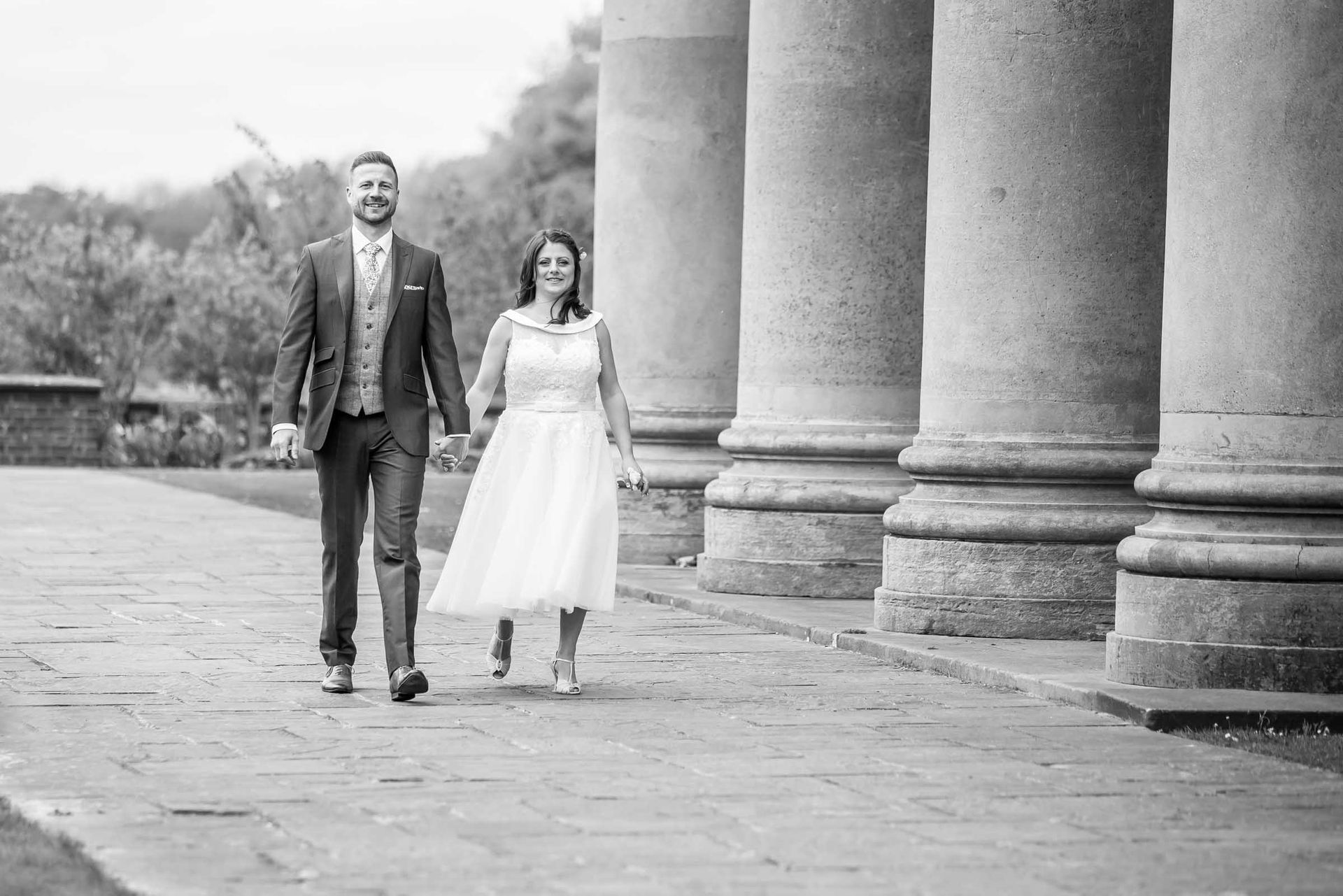 A black and white photo of a bride and groom walking down a sidewalk.