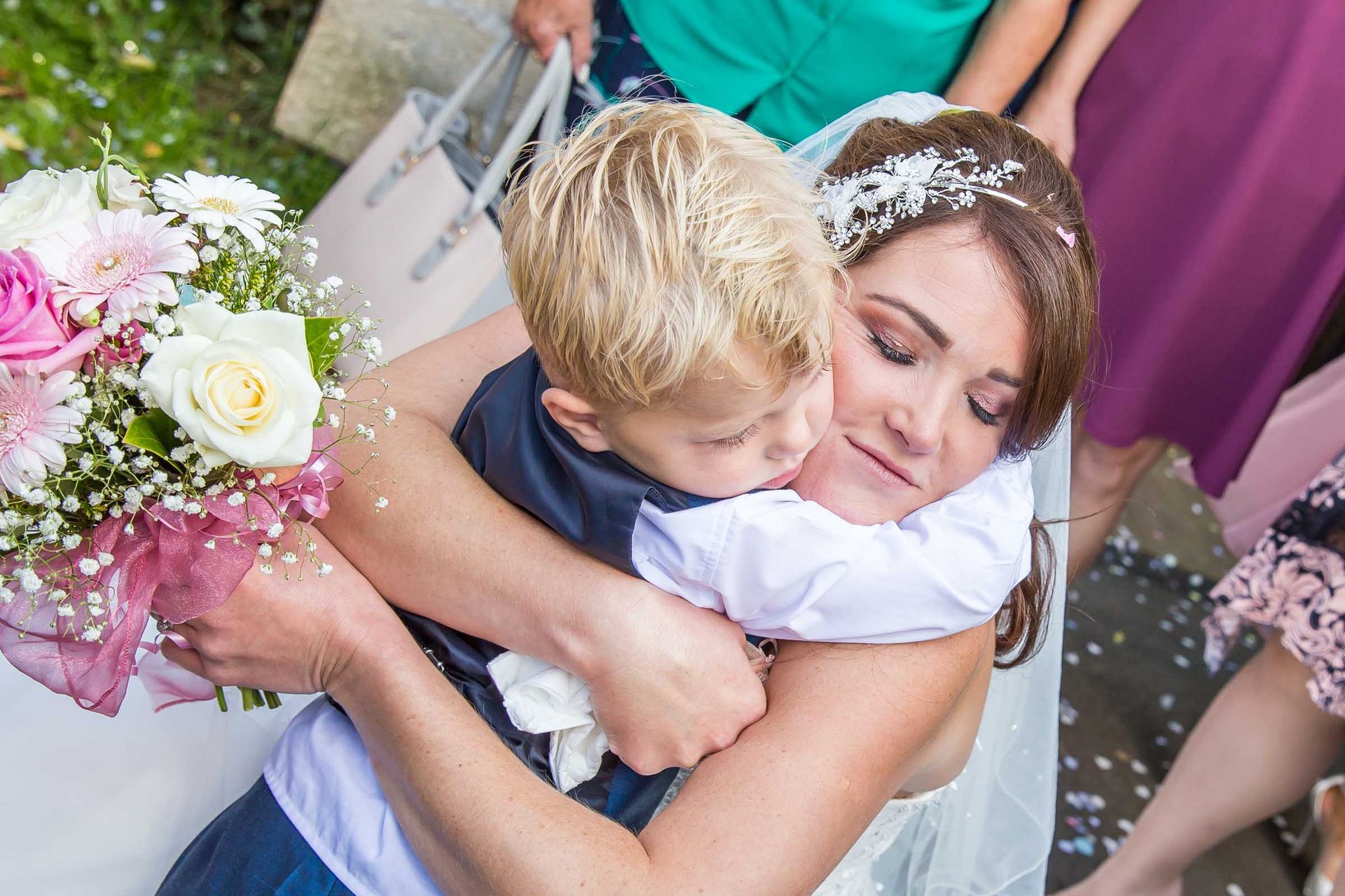 A woman in a wedding dress is hugging a little boy.