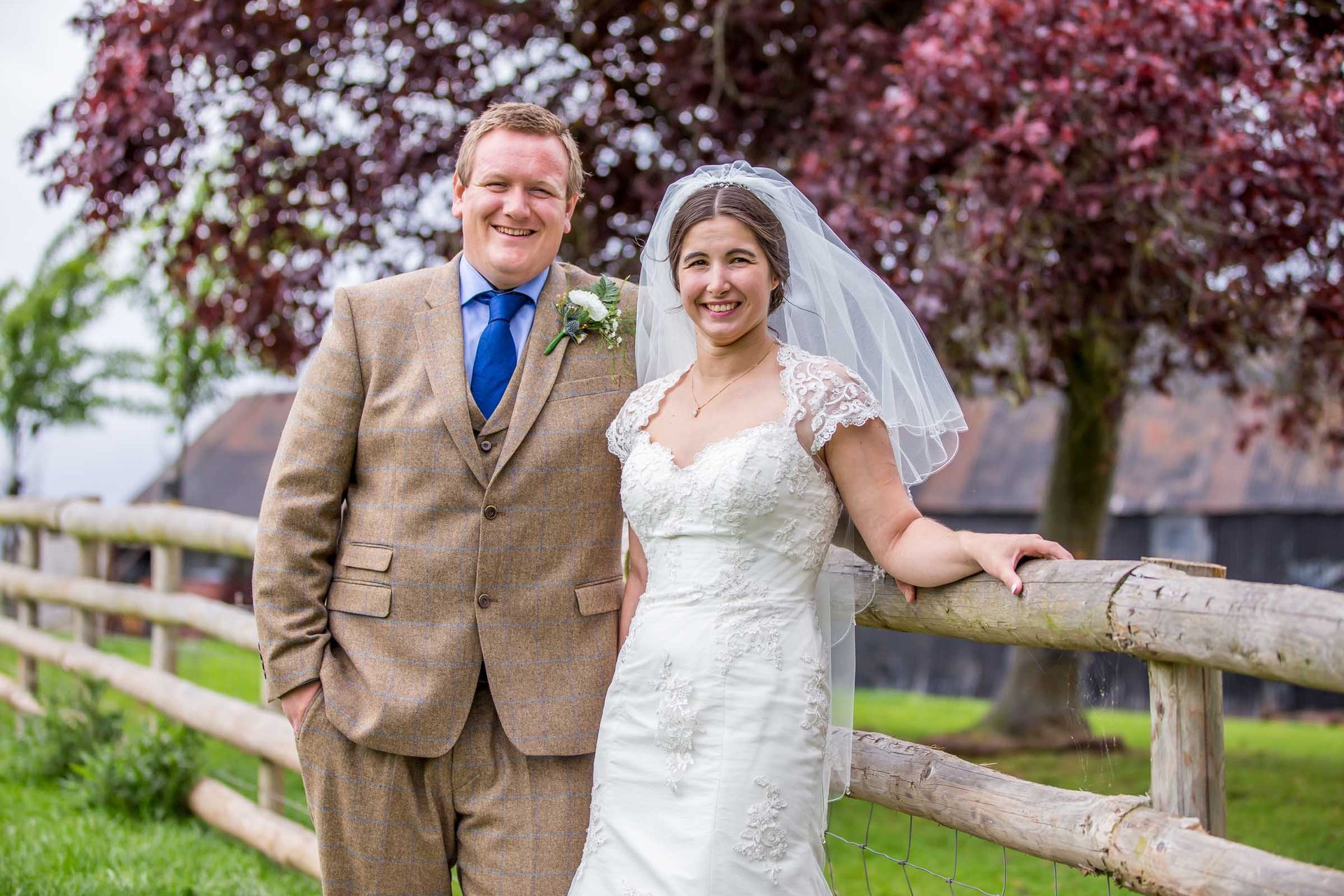 A bride and groom are posing for a picture next to a wooden fence.