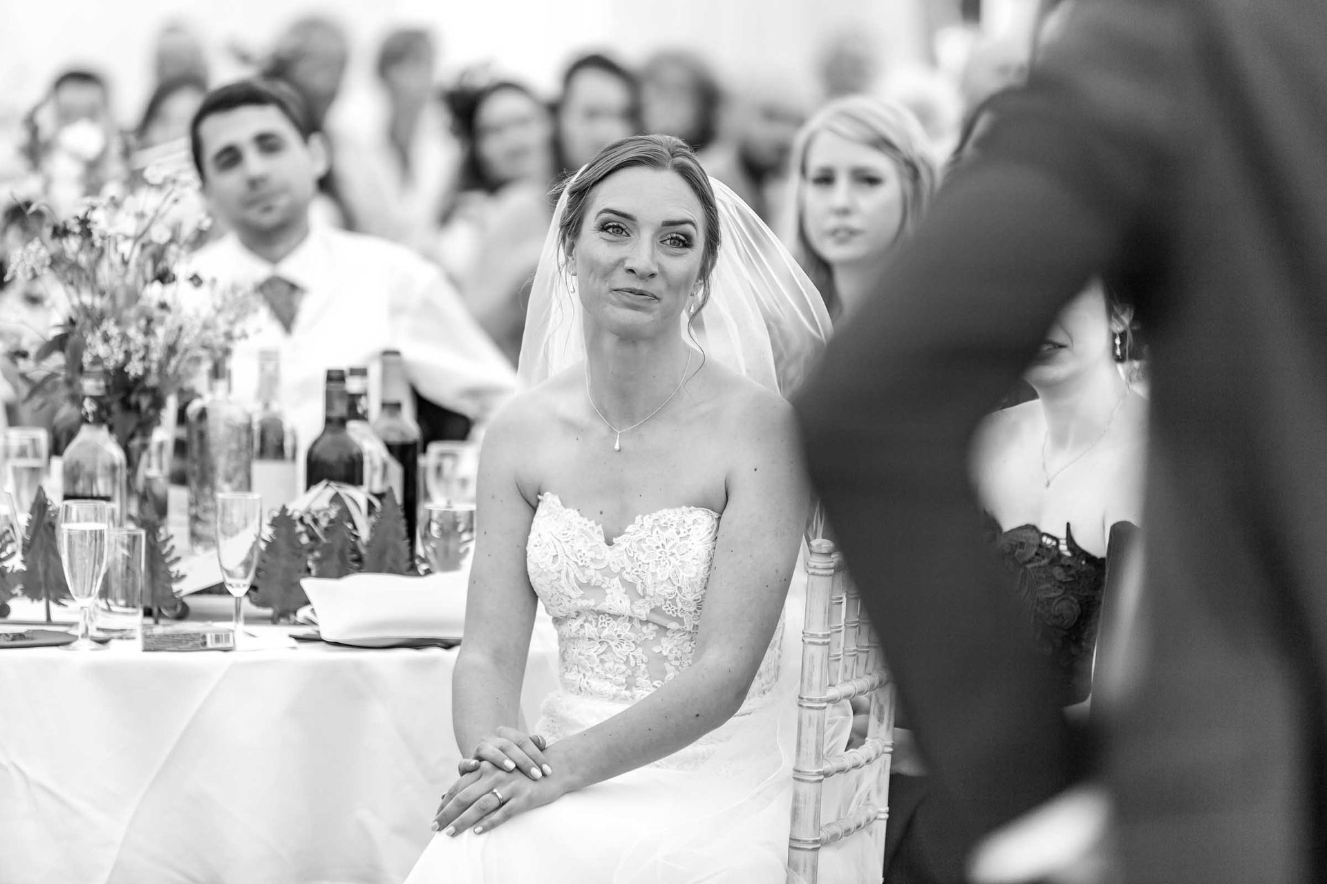A black and white photo of a bride sitting in a chair at a wedding reception.