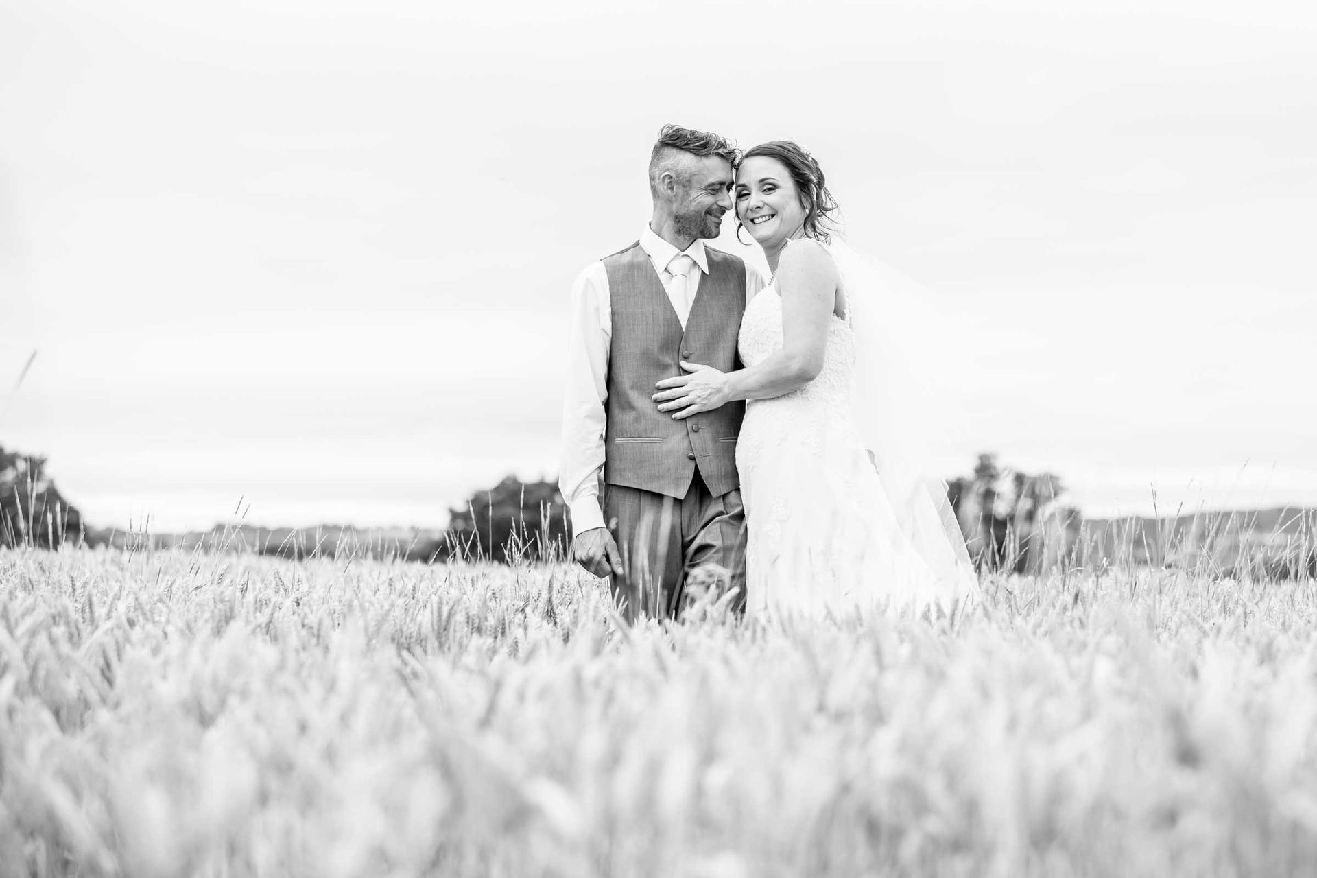 A bride and groom are standing in a field of wheat.