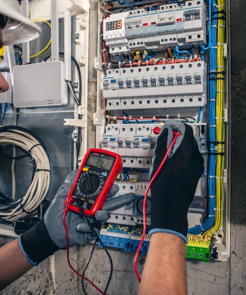An electrician is using a multimeter to test an electrical box.